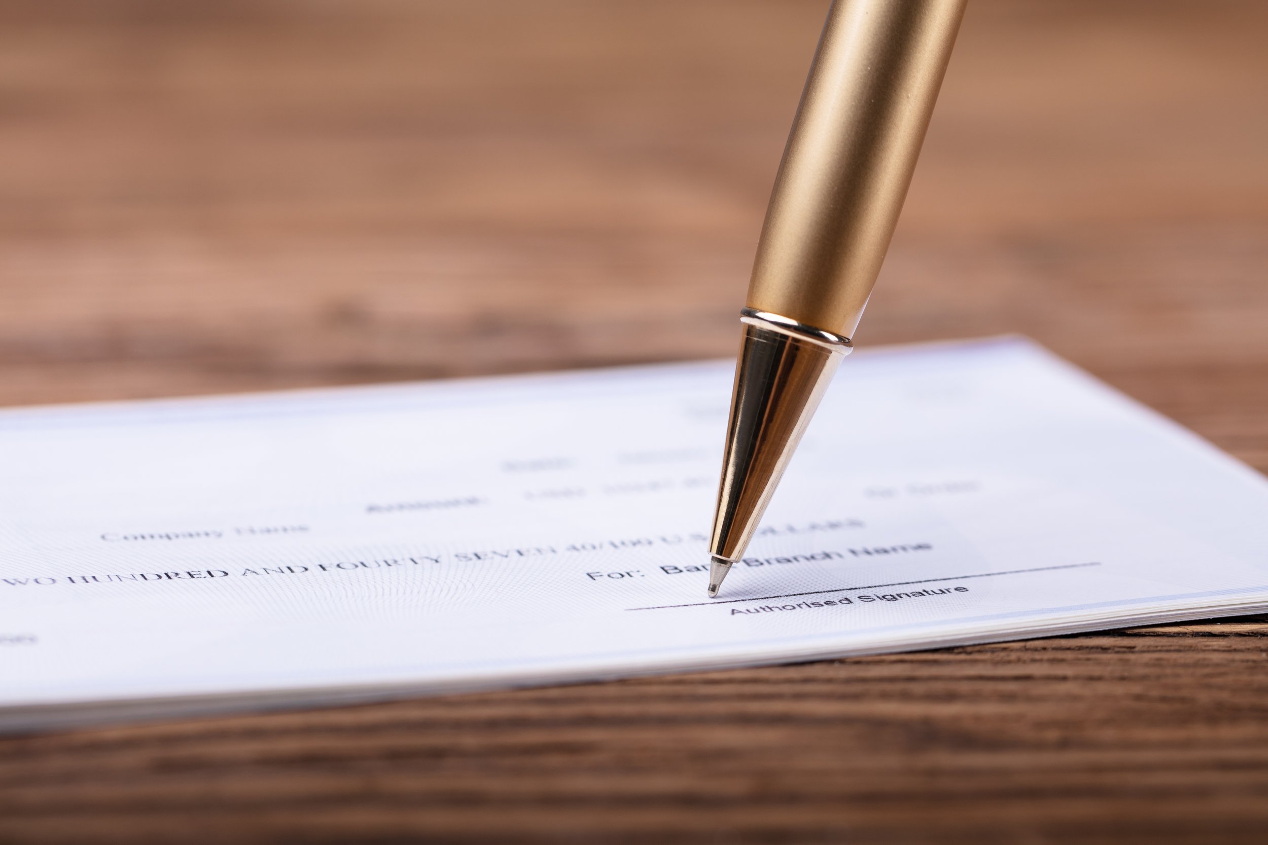 Close-up of a gold pen poised to sign a document on a wooden desk.