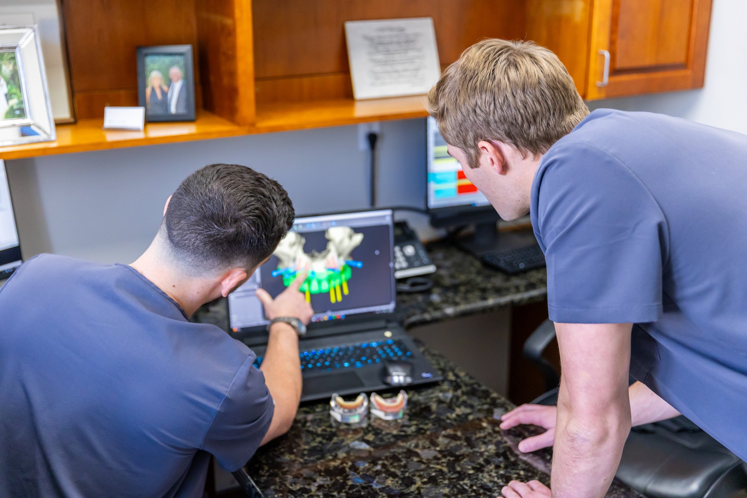 Two men in scrubs viewing a 3D model of a pelvis on a computer monitor, with one pointing at the screen.