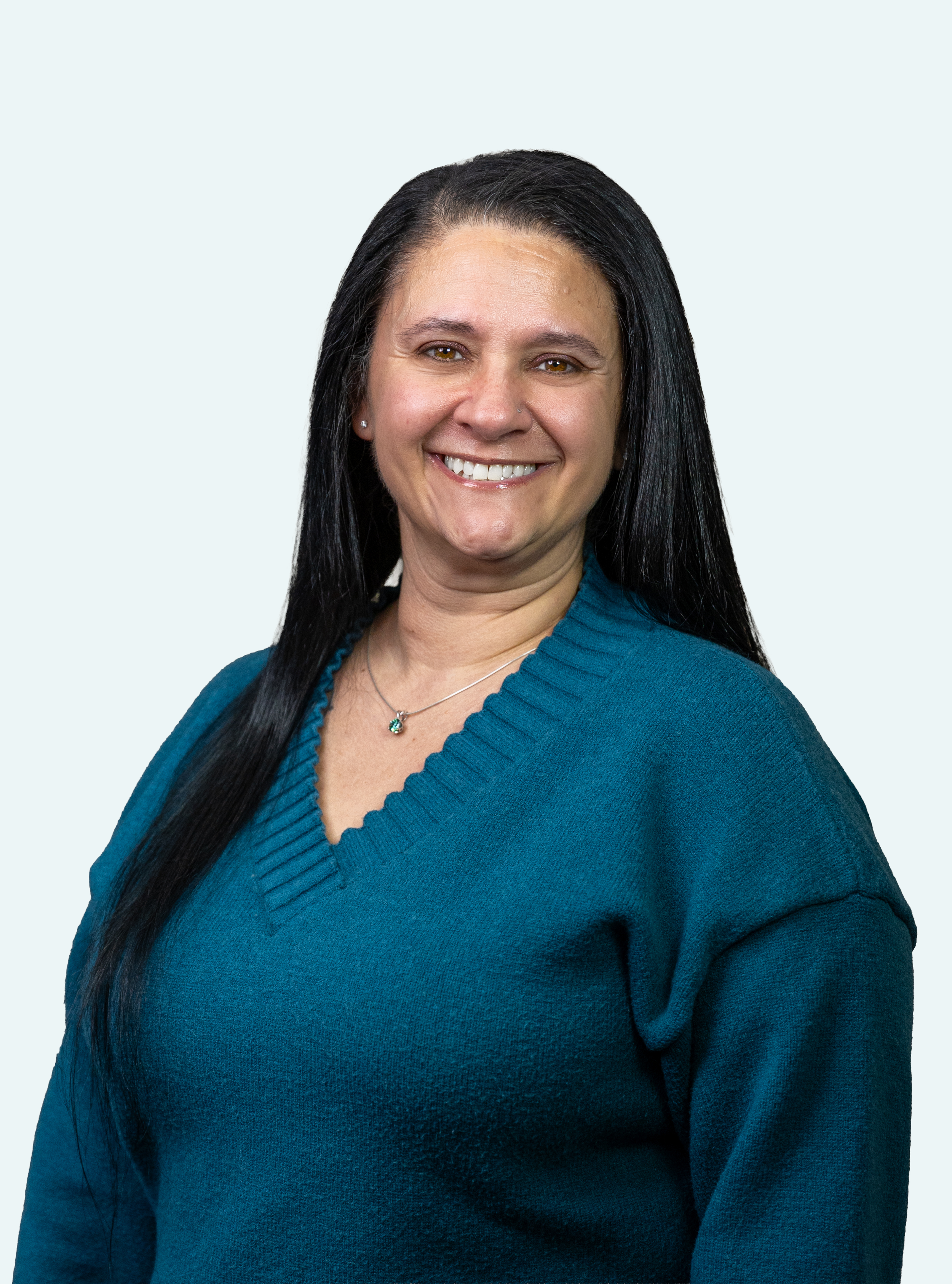 A smiling woman with long black hair wearing a blue sweater and a necklace.