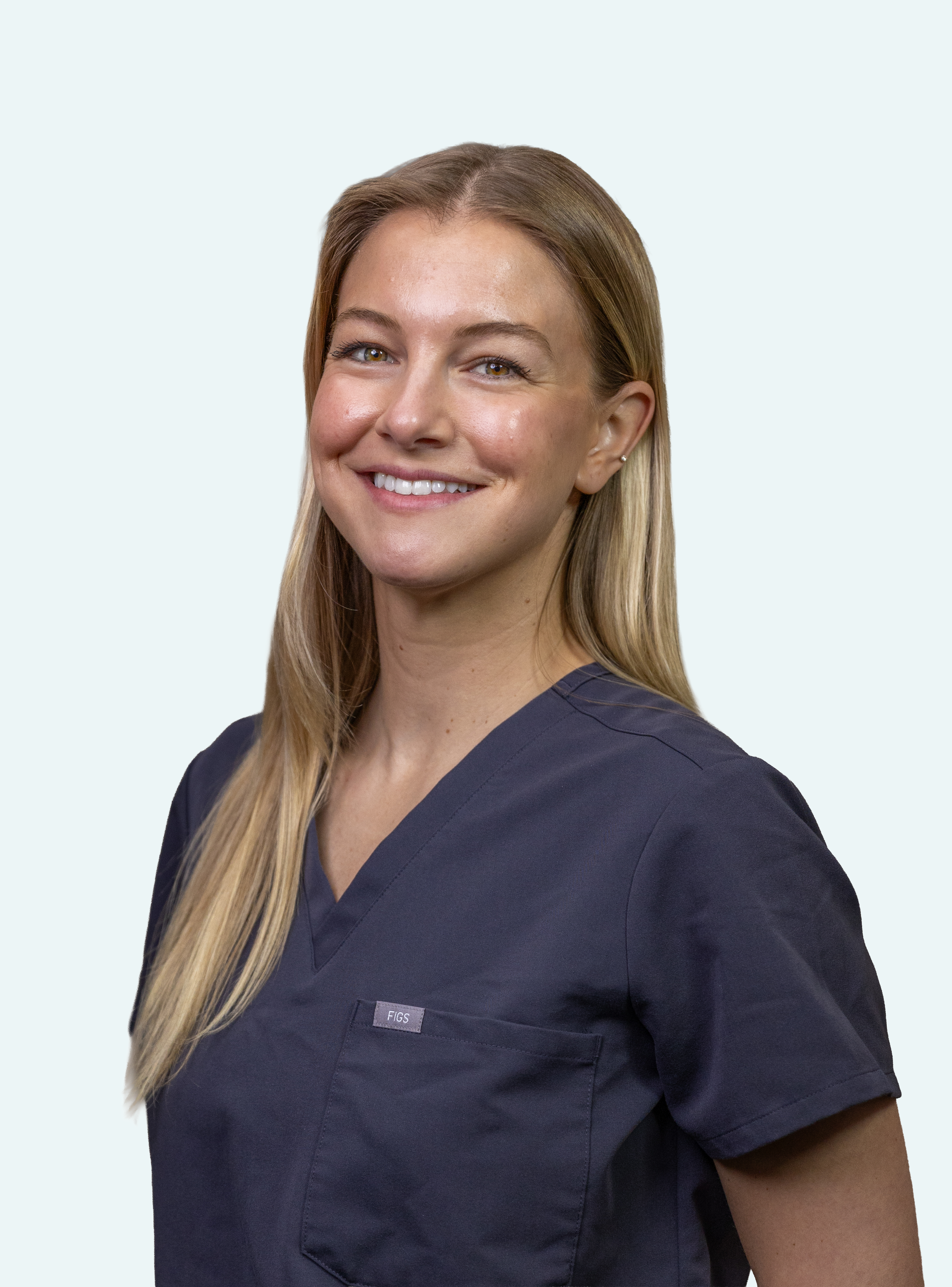 A woman with long blonde hair wearing navy medical scrubs smiling at the camera.