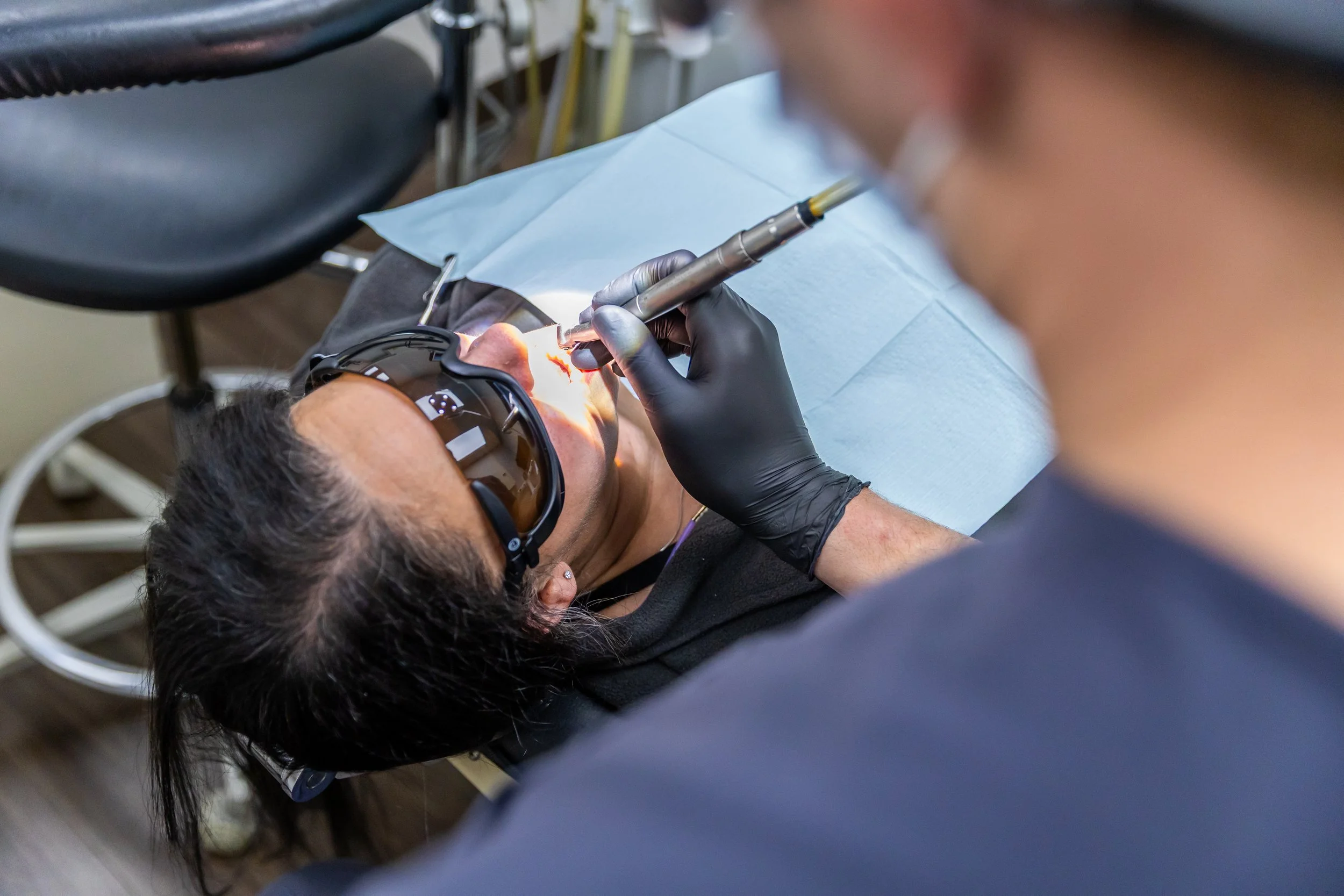 A person undergoing dental surgery while wearing protective sunglasses, with a dentist working on their mouth using a dental tool.
