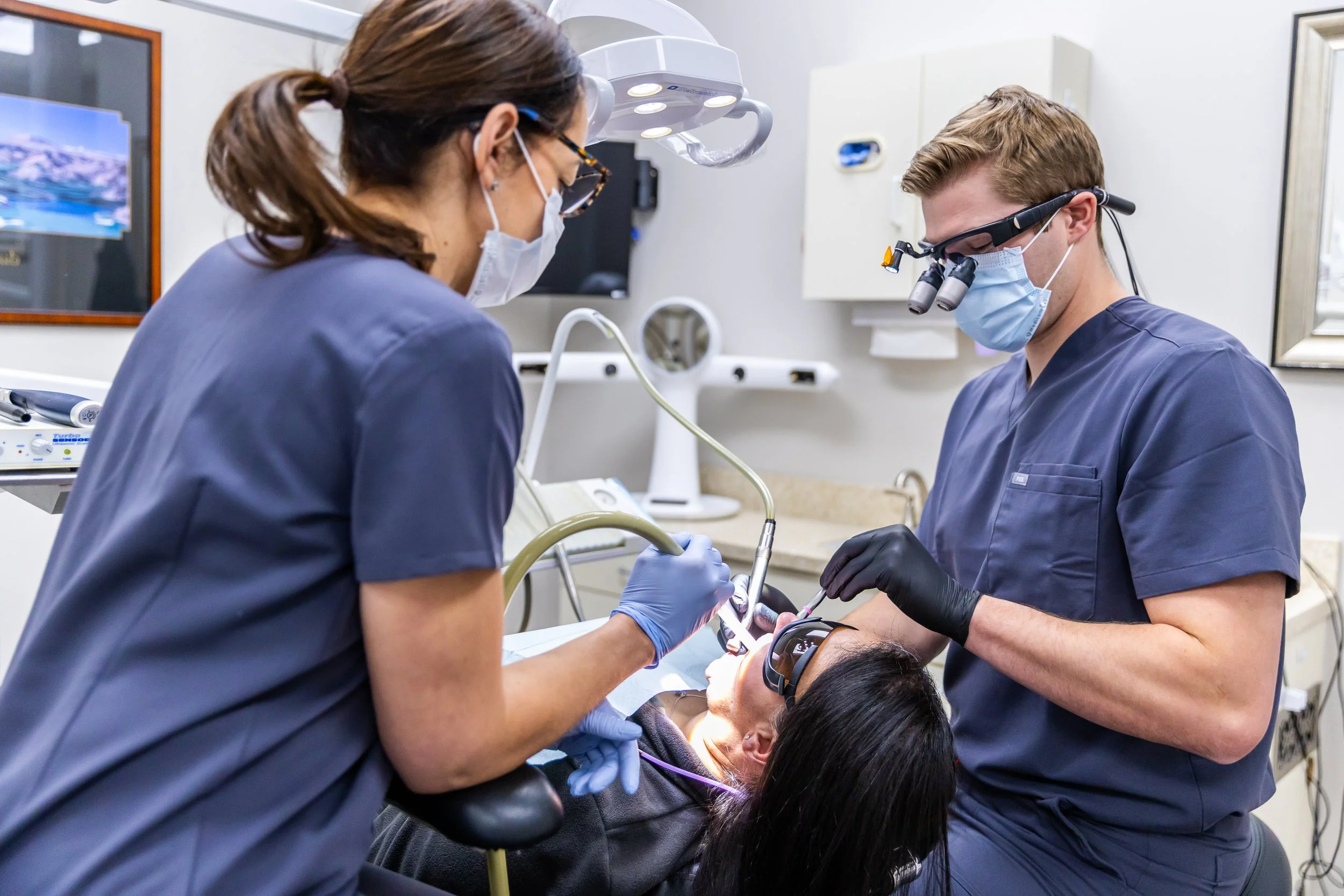 Dentists performing a dental procedure on a patient in an examination room.