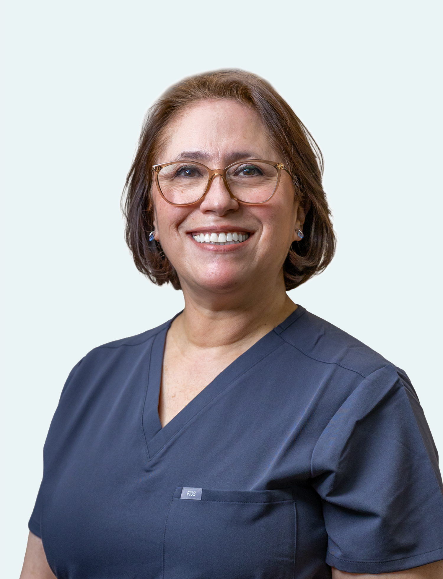 A smiling woman with short brown hair, wearing glasses and navy medical scrubs, against a light background.