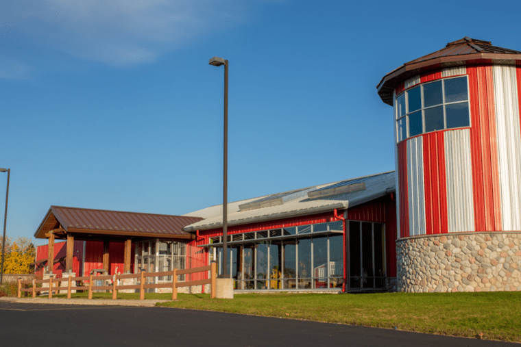 A red and silver striped building with a round tower, stone foundation, and large windows under a clear blue sky.