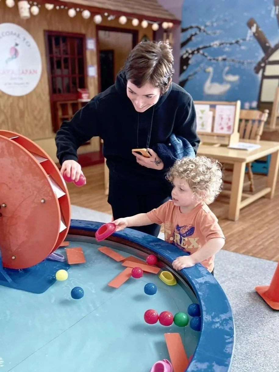 A woman and a young boy playing a table game with colorful balls and paddles in a cozy indoor setting.