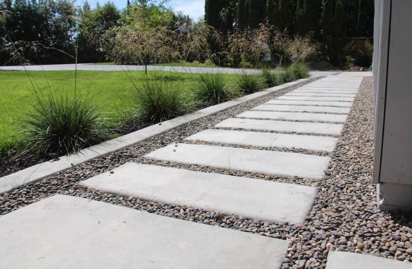 Concrete stepping stones on a gravel pathway, with a manicured lawn and ornamental grasses in the background.