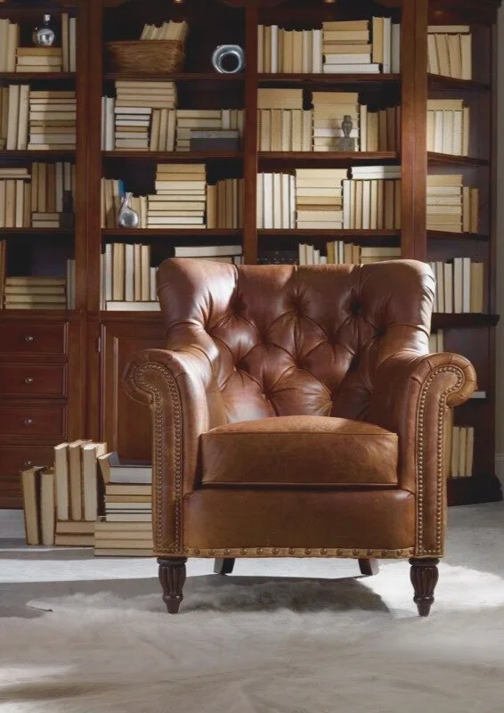 A cozy reading nook with a brown leather armchair in front of built-in wooden bookshelves filled with books.