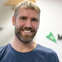 Peter, wearing a blue T-shirt, standing indoors with a plain background.