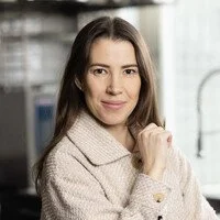 Erica wearing a beige sweater, standing indoors with a confident expression.