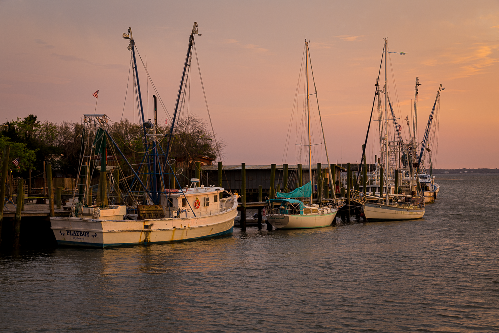 Several boats docked at a pier during sunset with a pink-hued sky and calm water. Photography Classes in Charleston SC. Camera Classes in Charleston SC