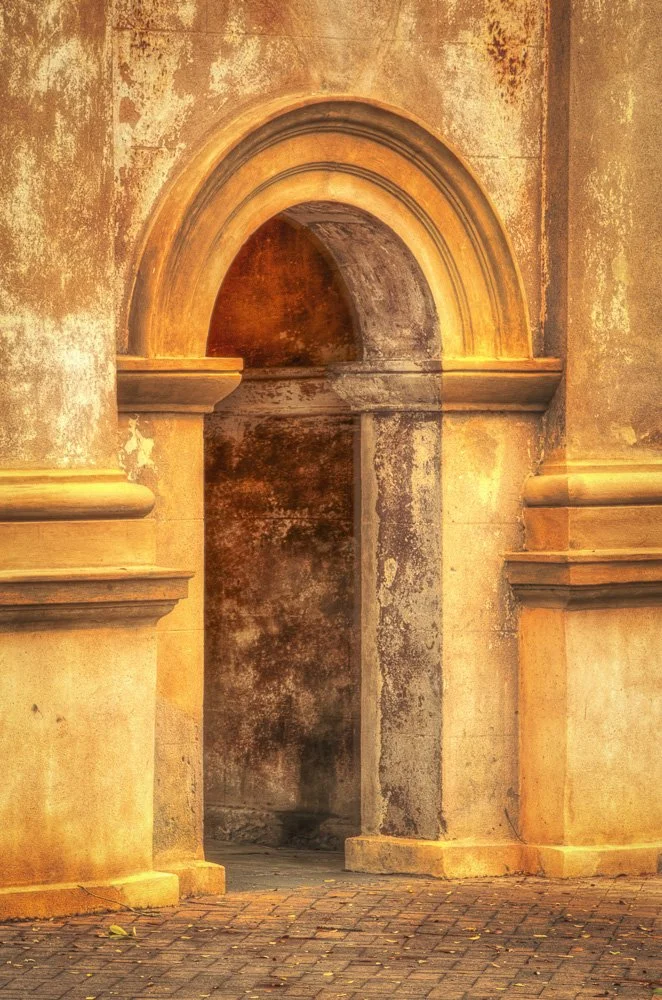 Old, weathered stone wall with arched doorway and decorative molding, illuminated by warm light.