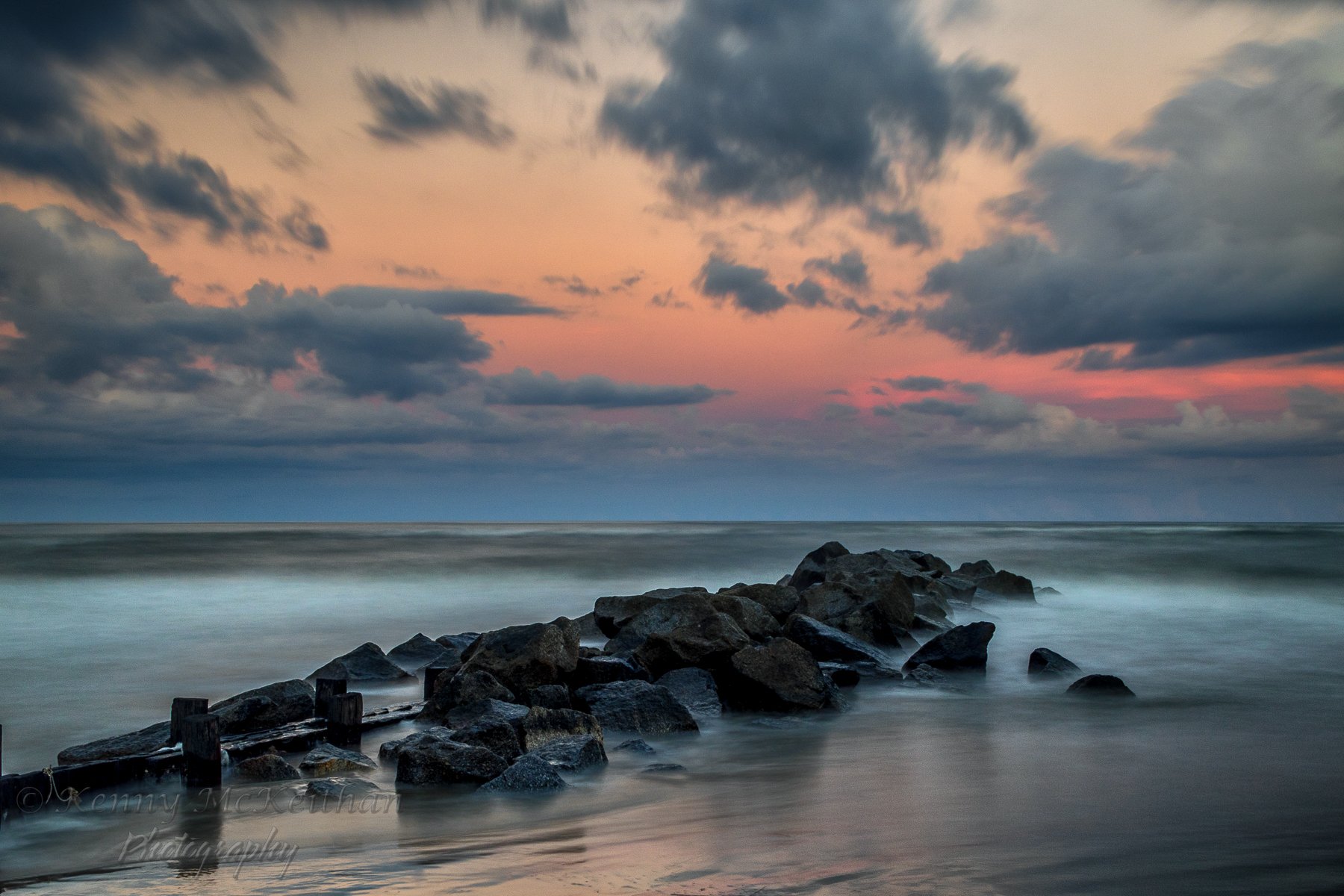 A rocky jetty extending into the ocean during sunset with colorful clouds in the sky. Photography Classes in Charleston SC. Camera Classes in Charleston SC