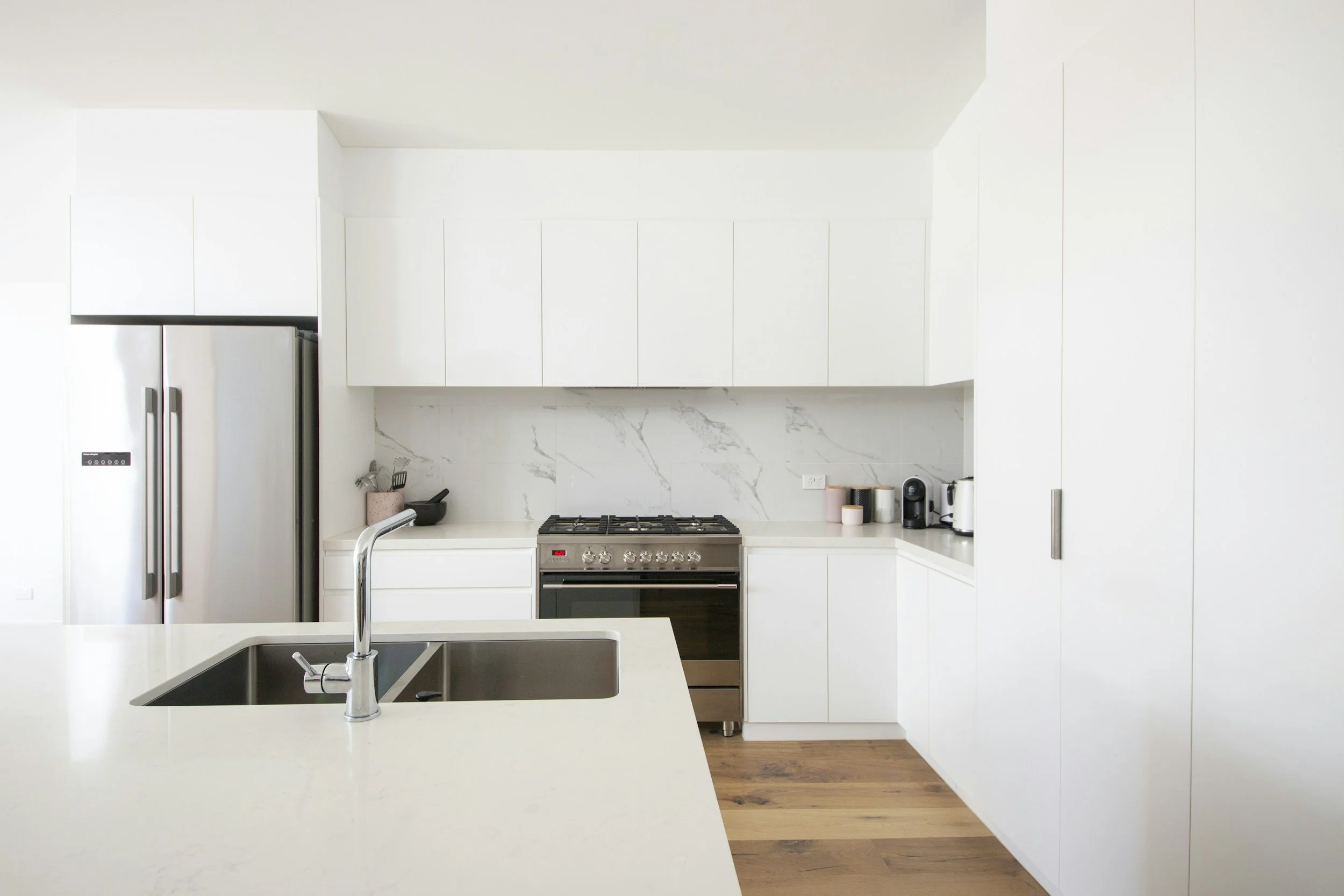 Bright modern white kitchen with slab cabinetry, quartz countertops, marble-look backsplash, and integrated island sink