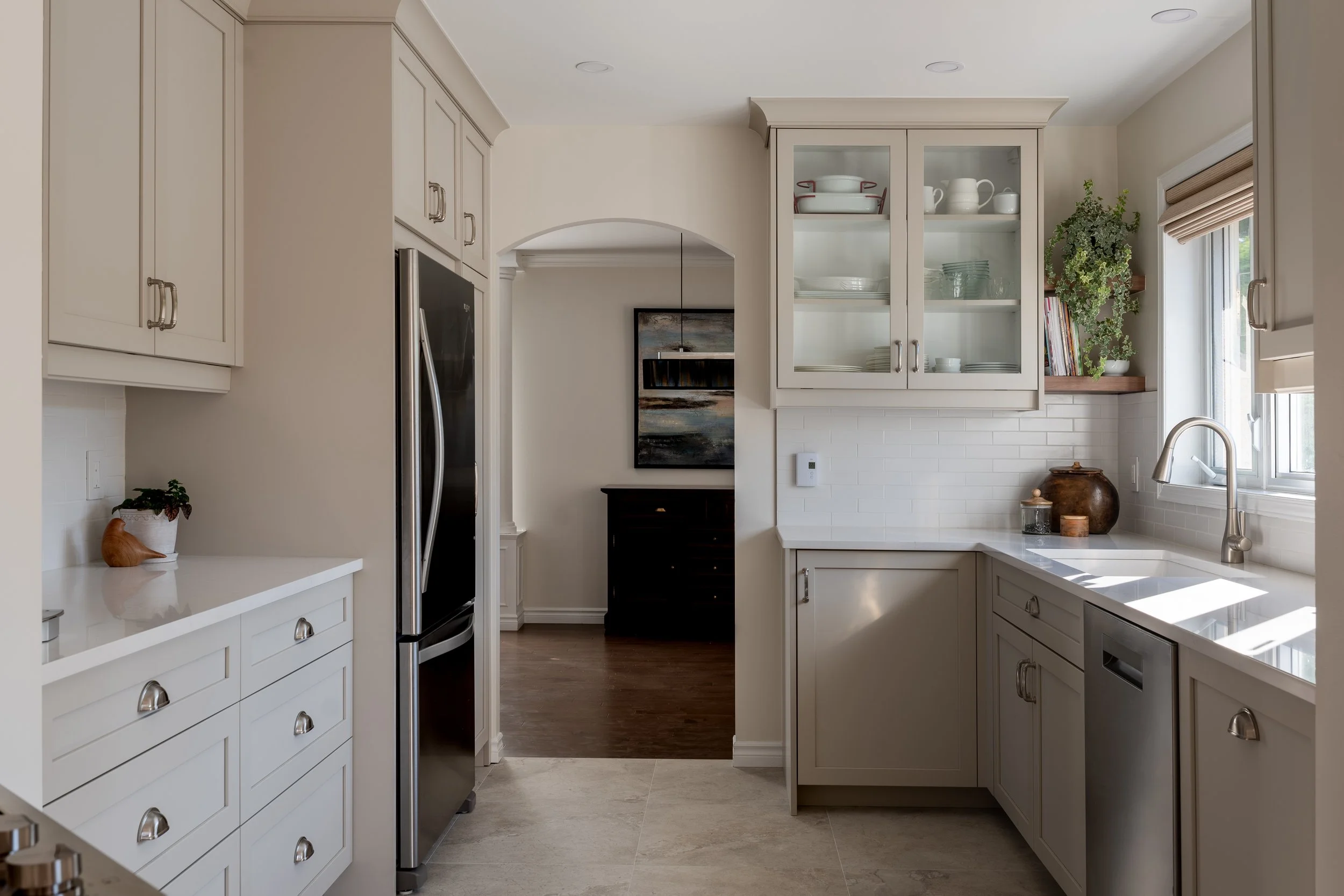 Bright neutral-toned shaker kitchen featuring glass-front cabinetry, white quartz countertops, stainless steel appliances, and a glossy subway tile backsplash.