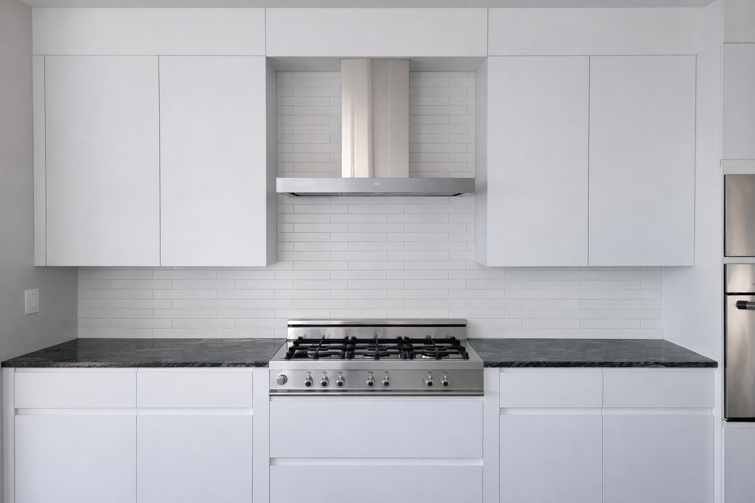 Contemporary white kitchen featuring J-pull cabinetry, dark stone countertops, stainless steel range and hood, and matte white subway tile.