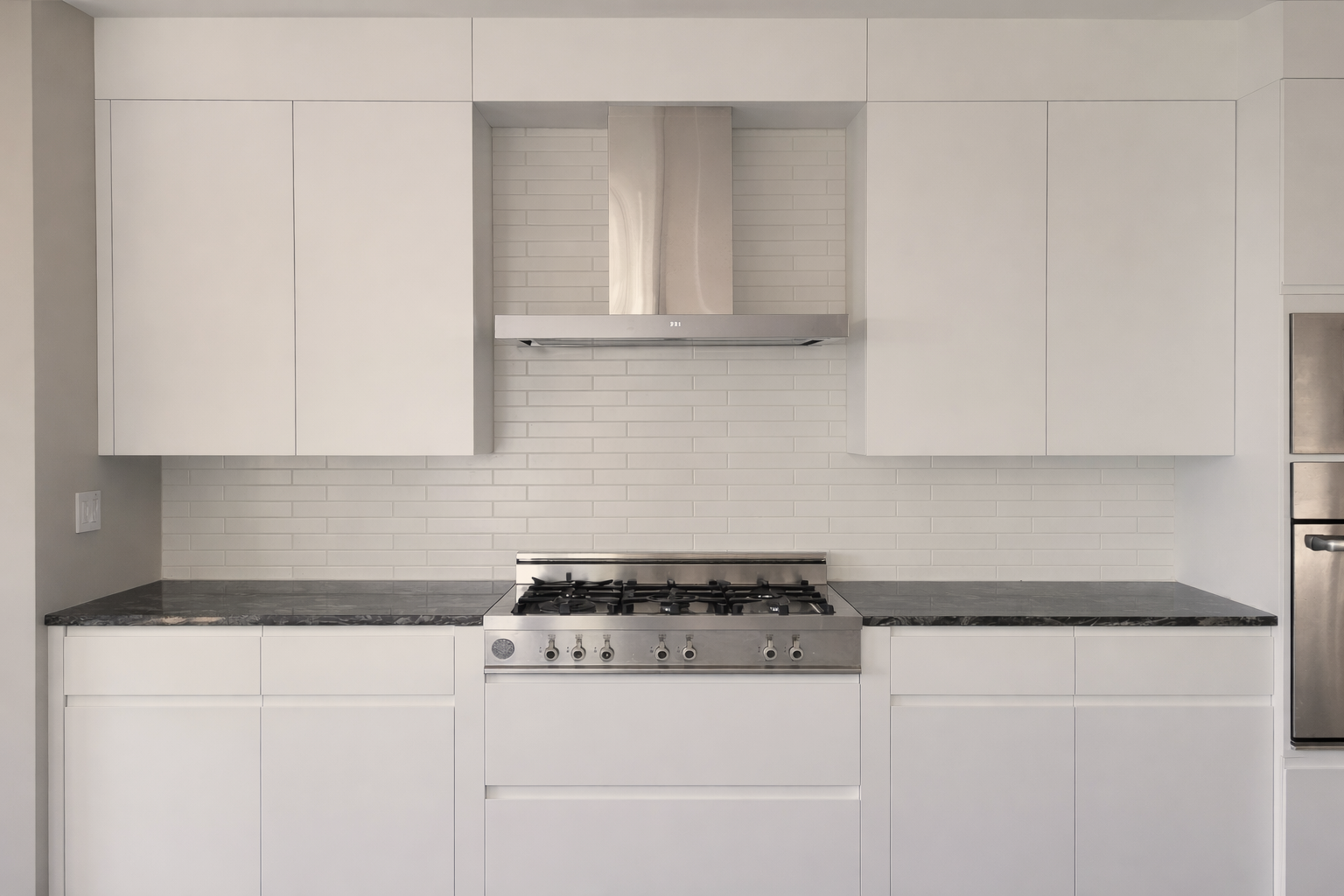 Cuisine blanche contemporaine avec armoires à prise en J et moulures affleurantes ajustées au plafond, comptoirs en pierre foncée, hotte en acier inoxydable et dosseret en céramique métro mate.