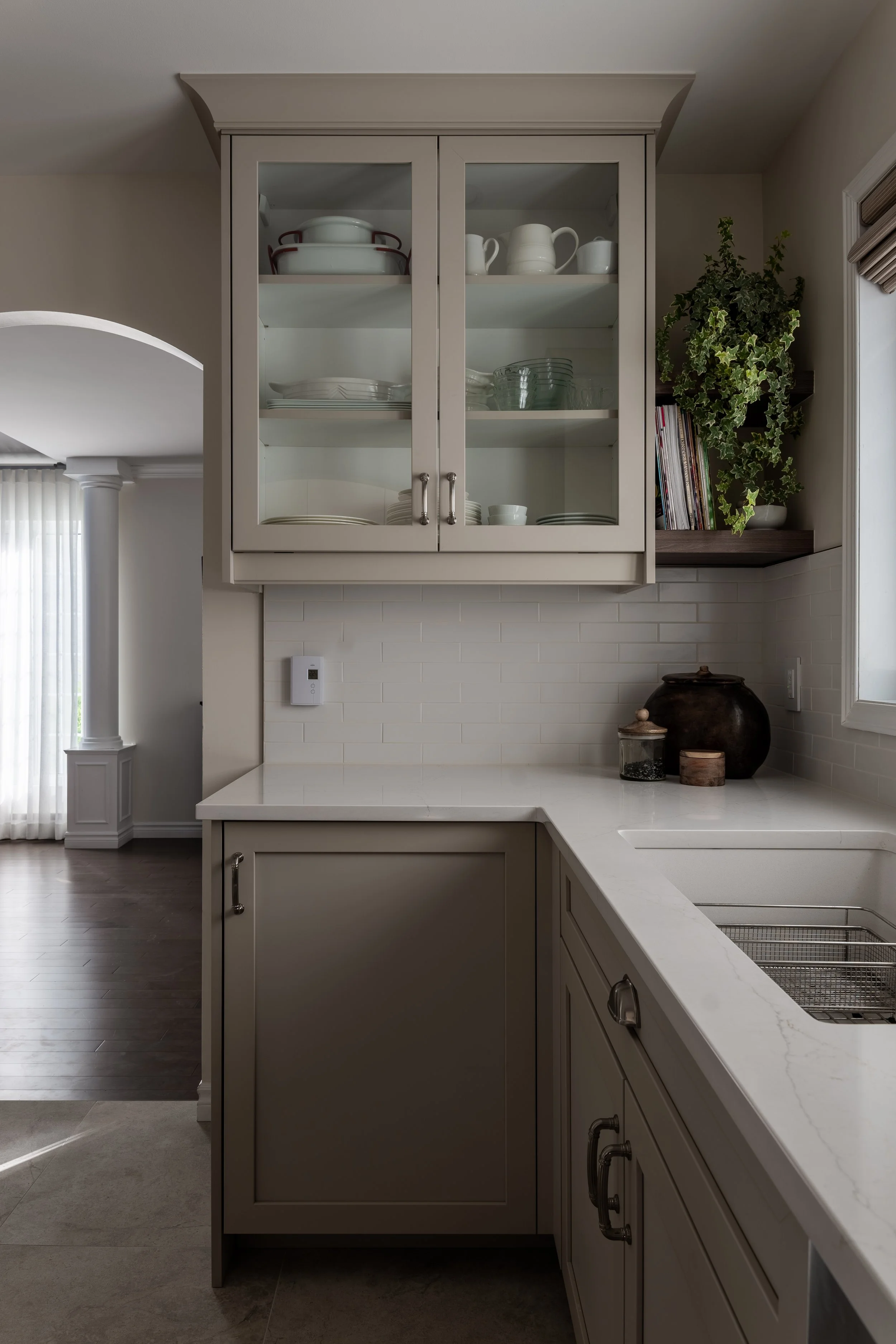 Neutral-toned shaker kitchen with glass display cabinets, white quartz countertops, and glossy subway tile backsplash.