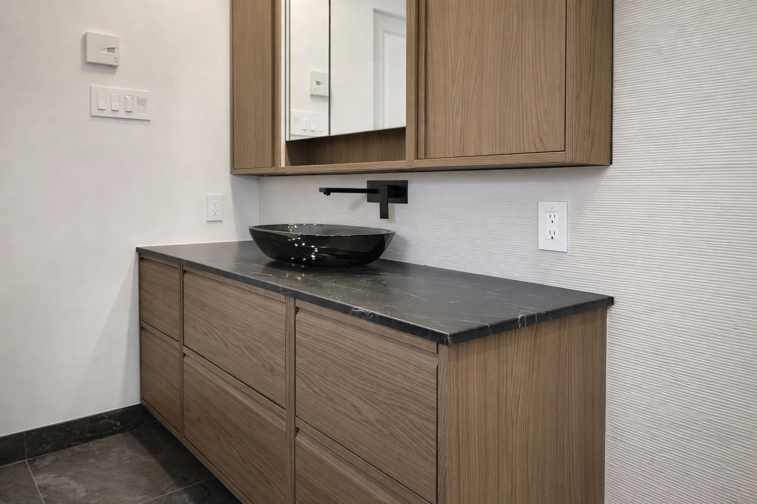 Modern bathroom featuring walnut slab vanity, dark stone countertop, black vessel basin, and minimalist wall-mounted faucet.