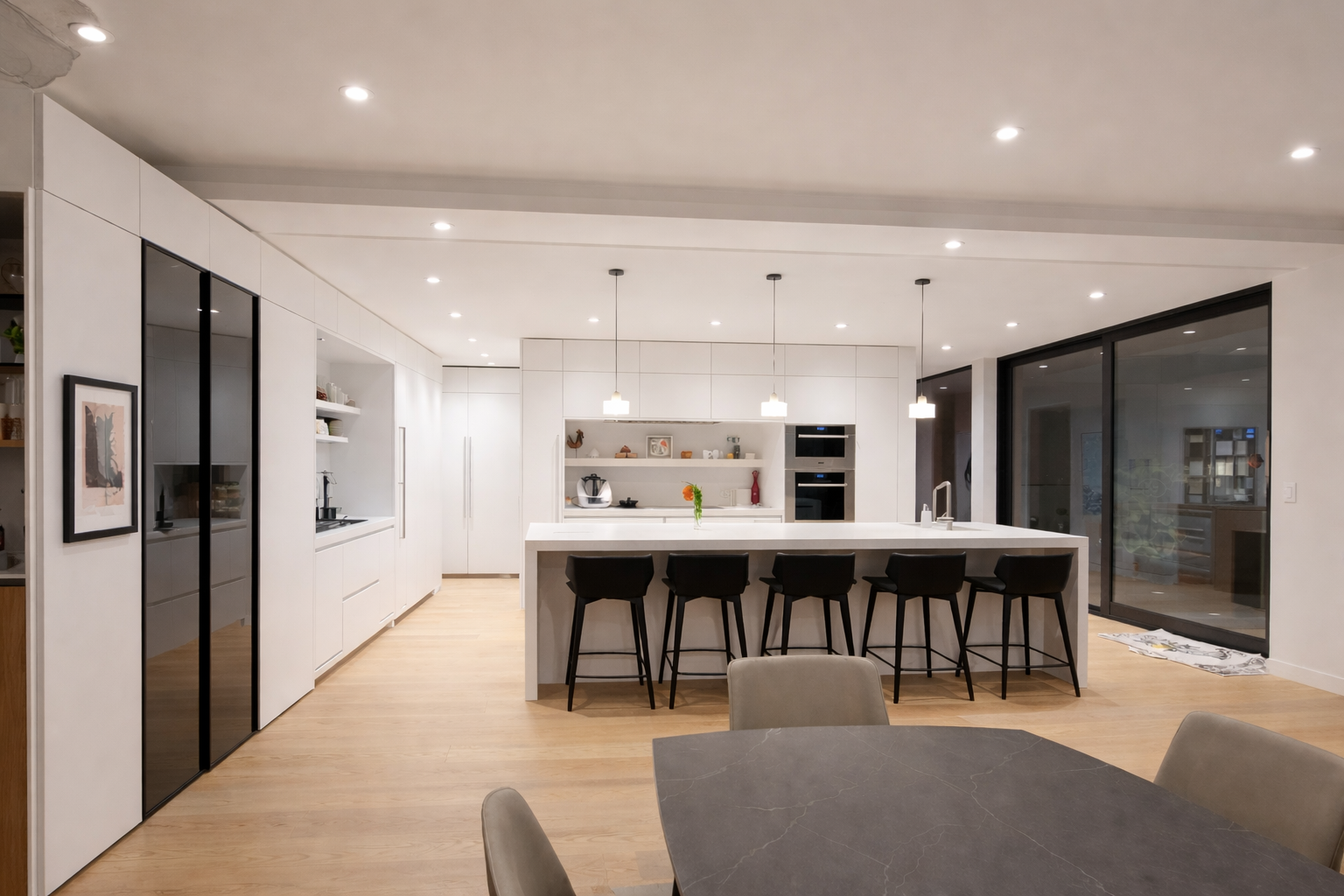 Contemporary open-concept kitchen with floor-to-ceiling flat-panel cabinetry, large waterfall island with seating, integrated appliances, and black-framed glass doors.