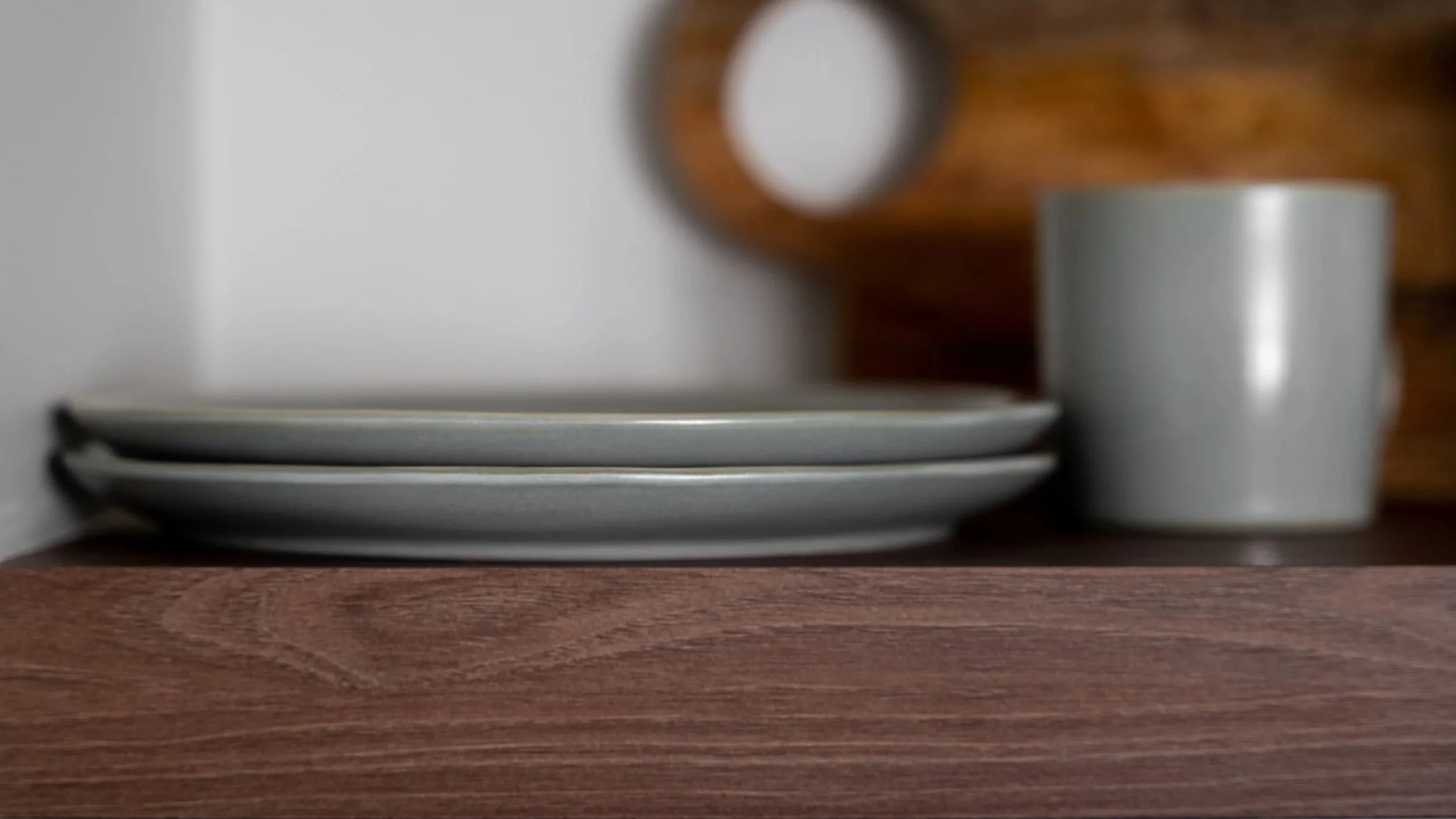 Walnut floating shelf with stacked stoneware plates and neutral ceramic mug.