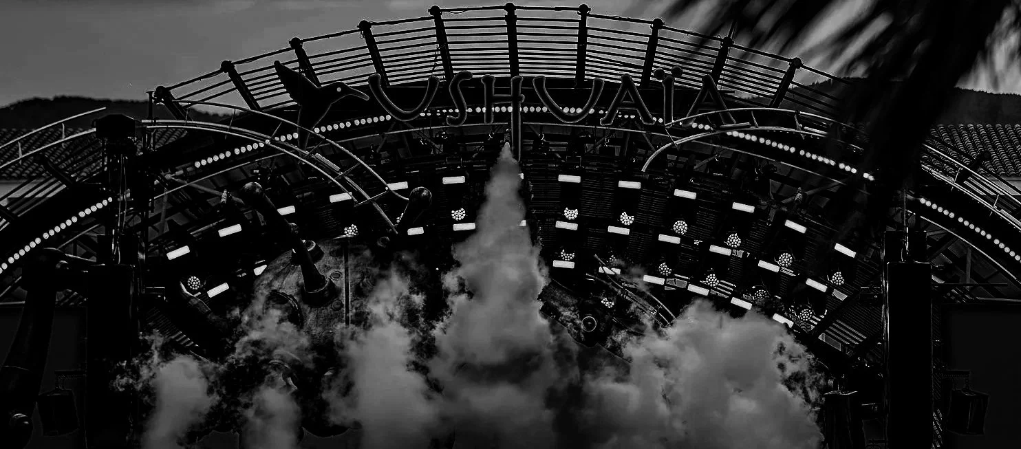 Stage set up with 'USHUAIA' sign, smoke effects, lighting, and DJ equipment at an outdoor event.