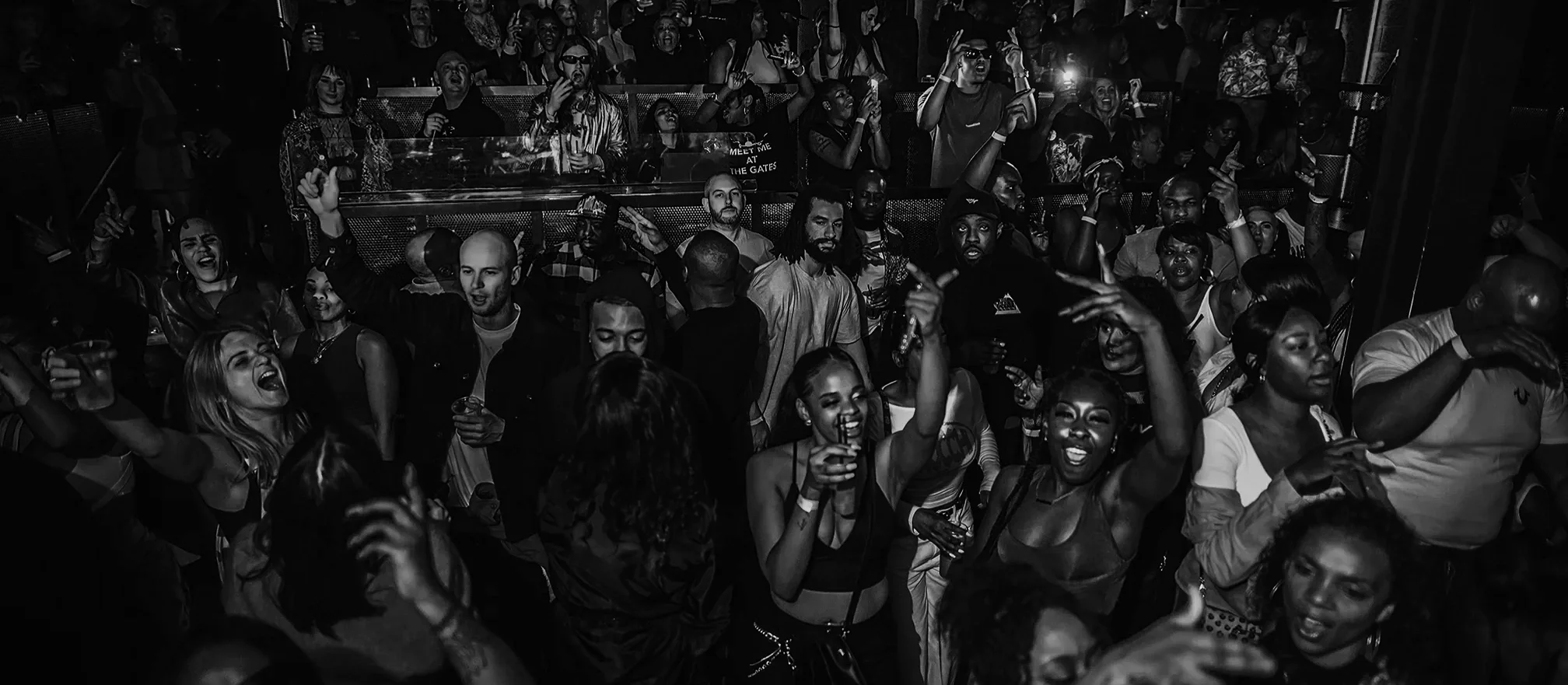 Crowd of people dancing and enjoying themselves at a nightclub with pink and red lighting.