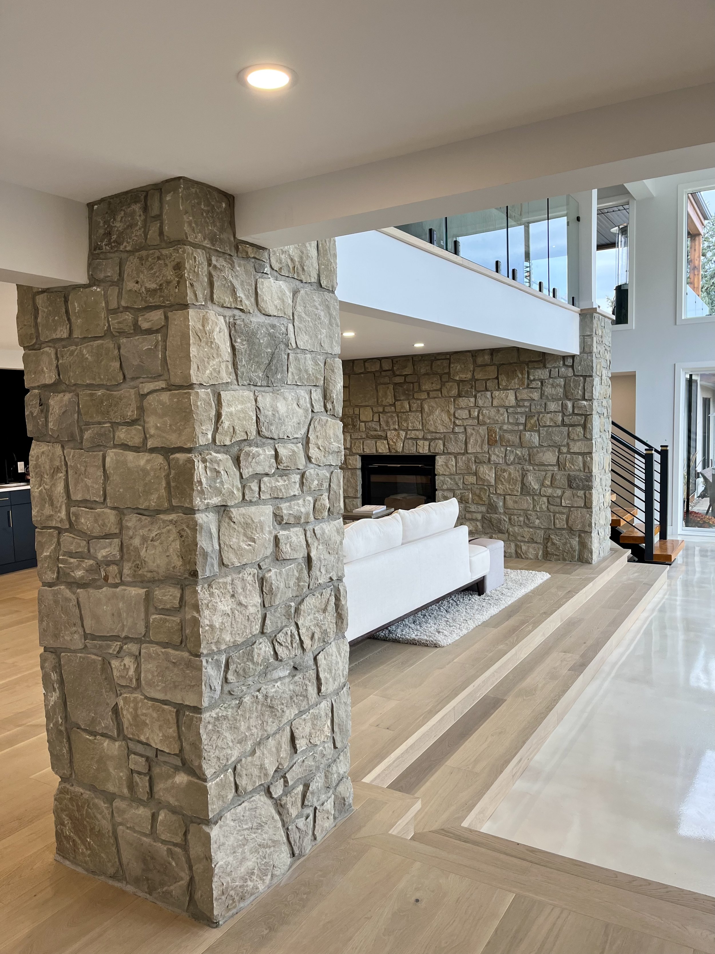 Modern living room with stone pillars, beige couch, and wooden flooring.