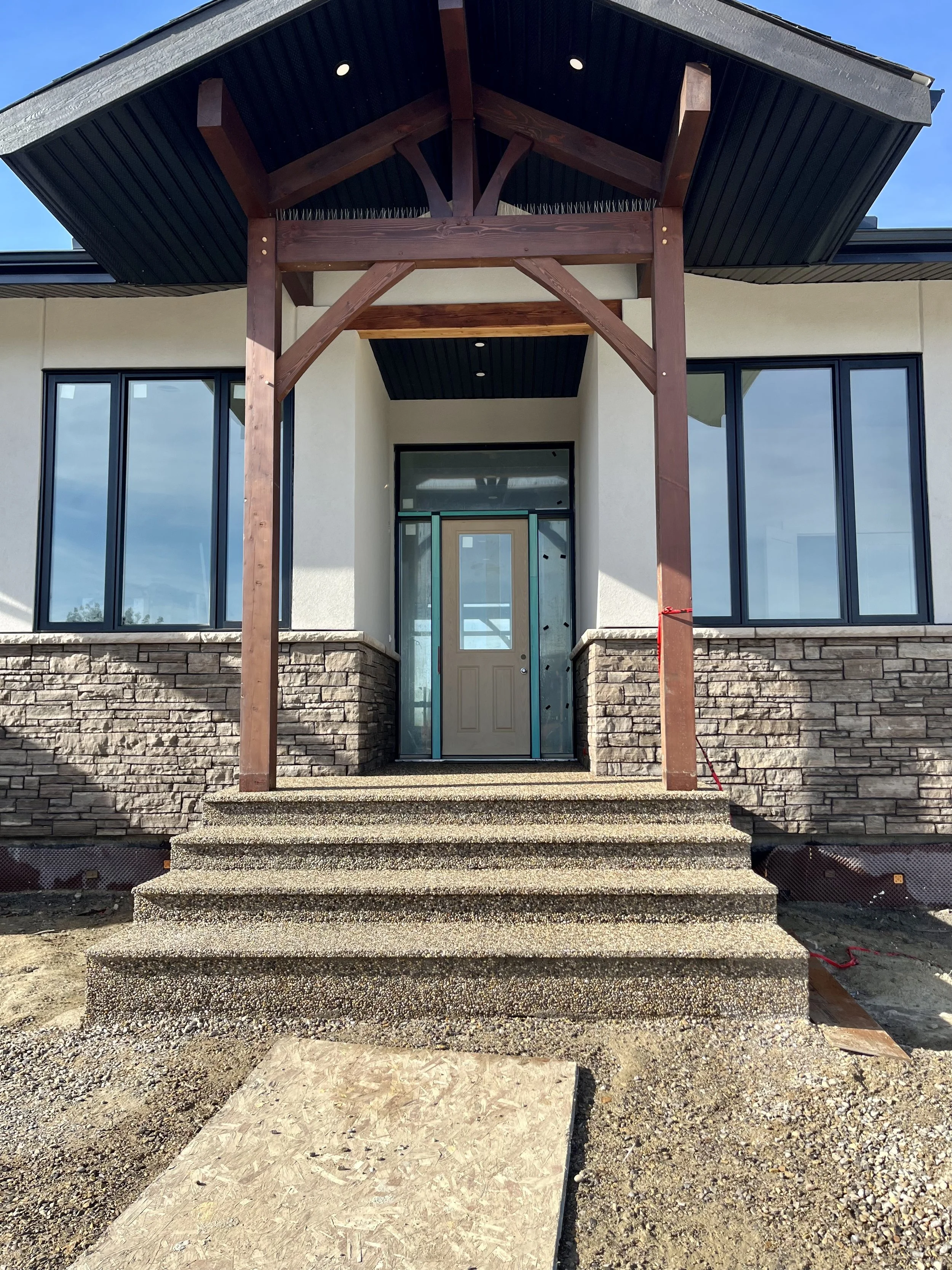 Front entrance of a house with a wooden porch, stone steps, and large windows.