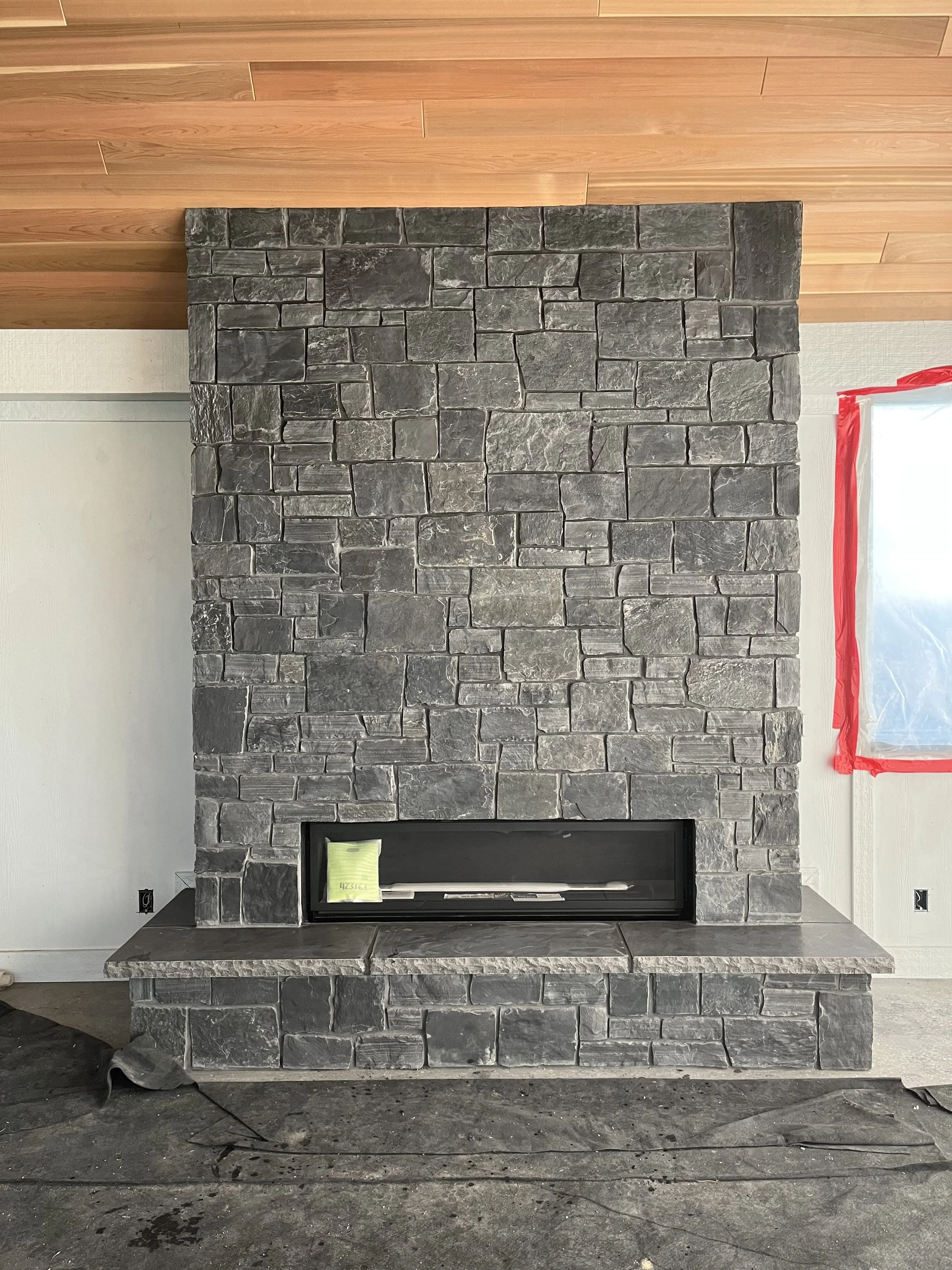 Modern stone fireplace with a rectangular opening, set against a wall with wood paneling above.