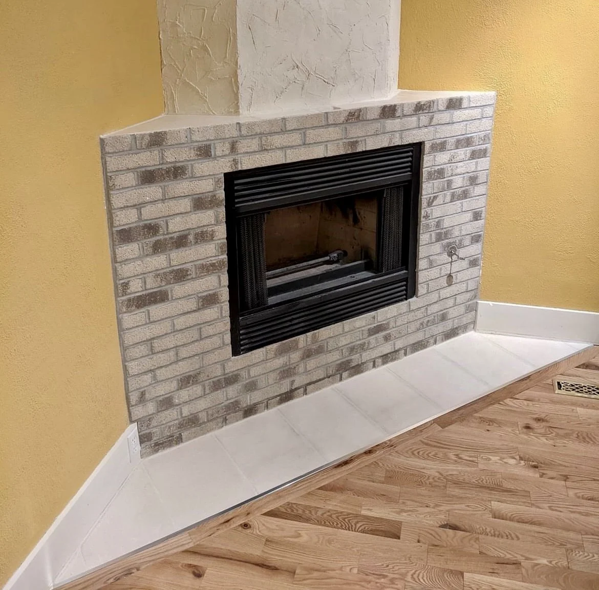 Brick fireplace with black metal frame in a room with yellow walls and hardwood floor.