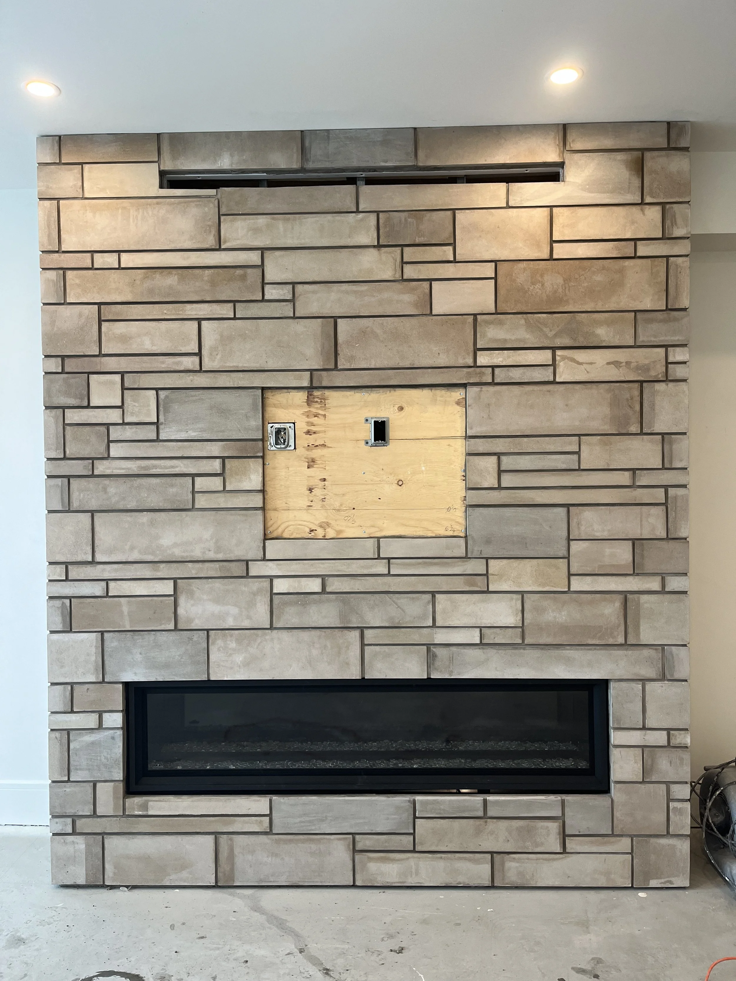 Stone brick fireplace wall with empty TV mount space above, recessed lighting.