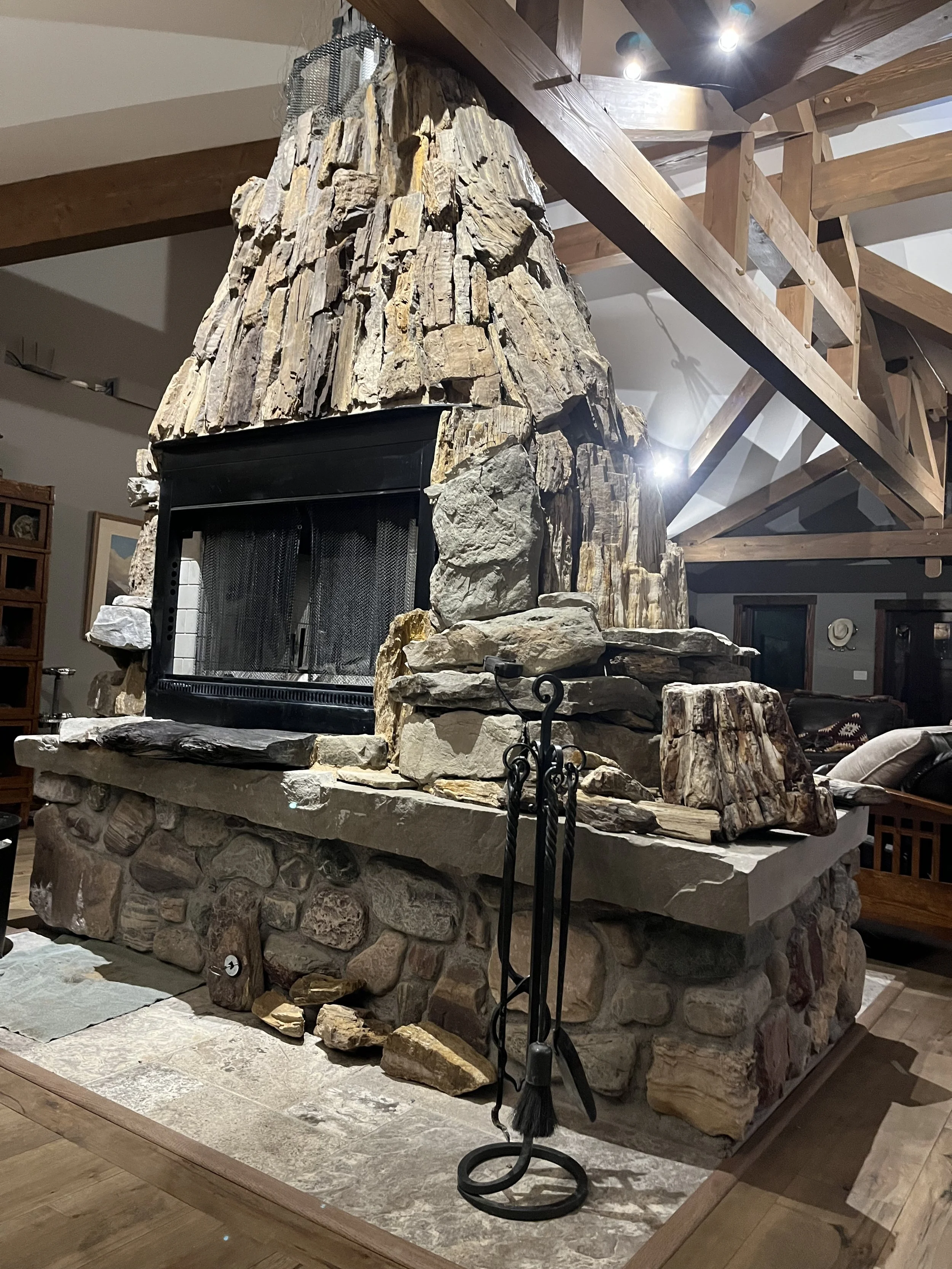 Stone fireplace with rustic design in a wooden interior, featuring fire tools set on the side.