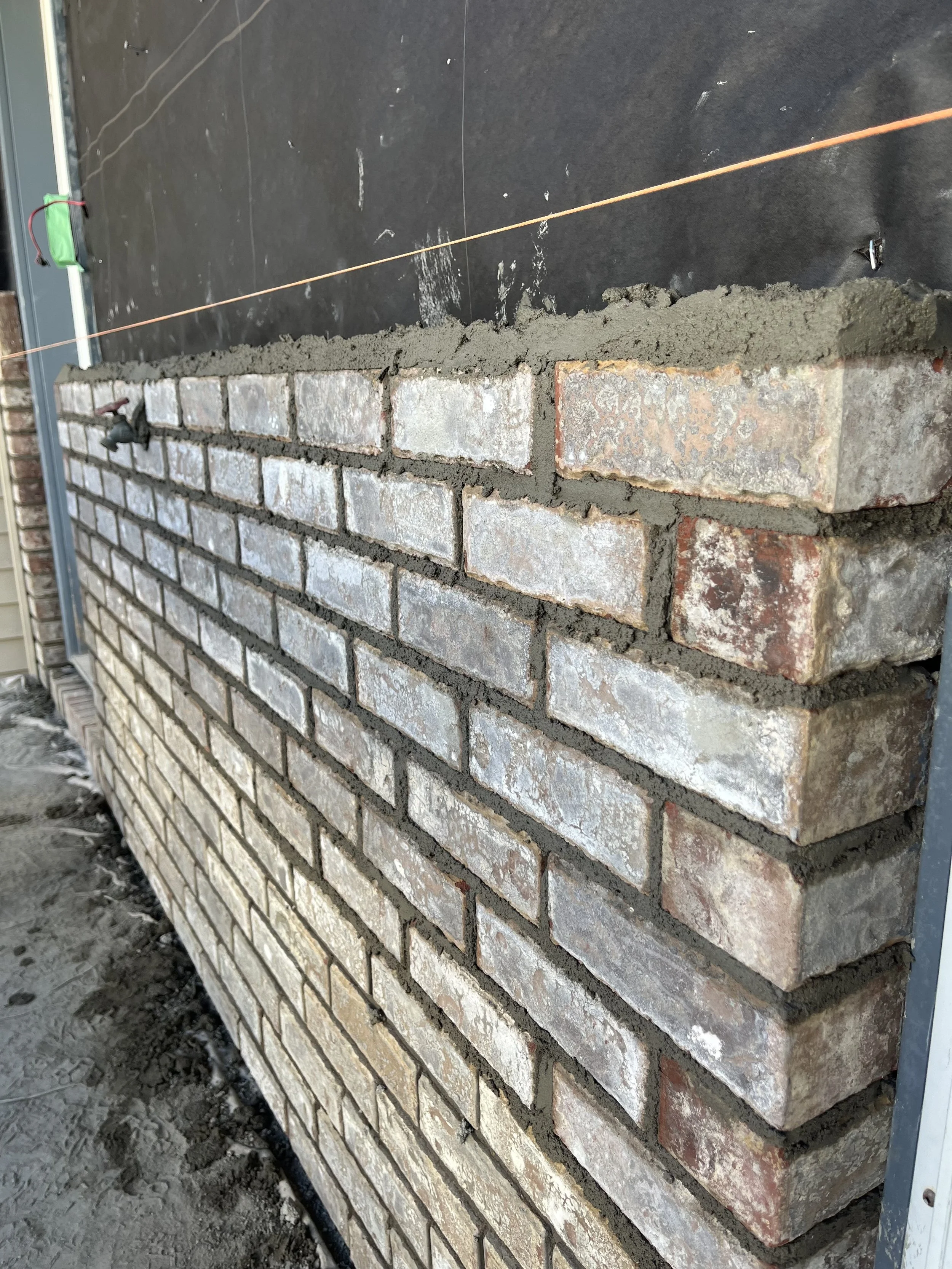 Close-up of a partially built brick wall with mortar, showing a guide string for alignment.