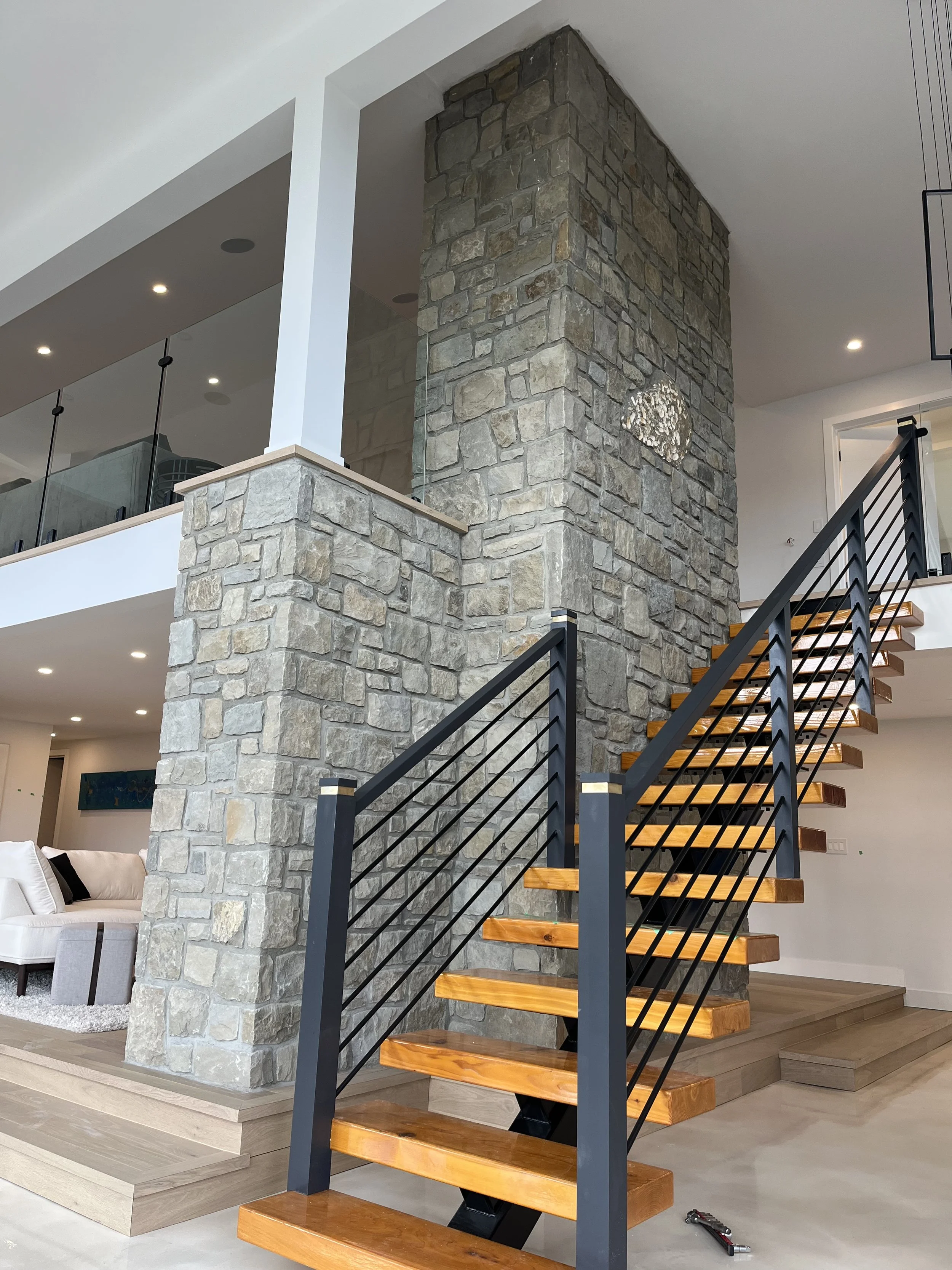 Interior view of a modern home with a wooden staircase and a stone fireplace wall.