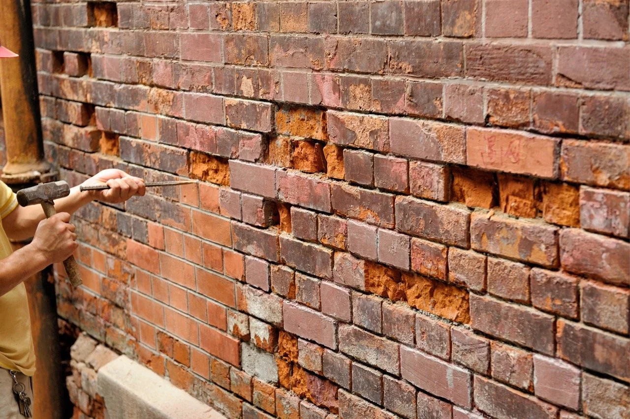 Person repairing damaged brick wall with hammer and chisel