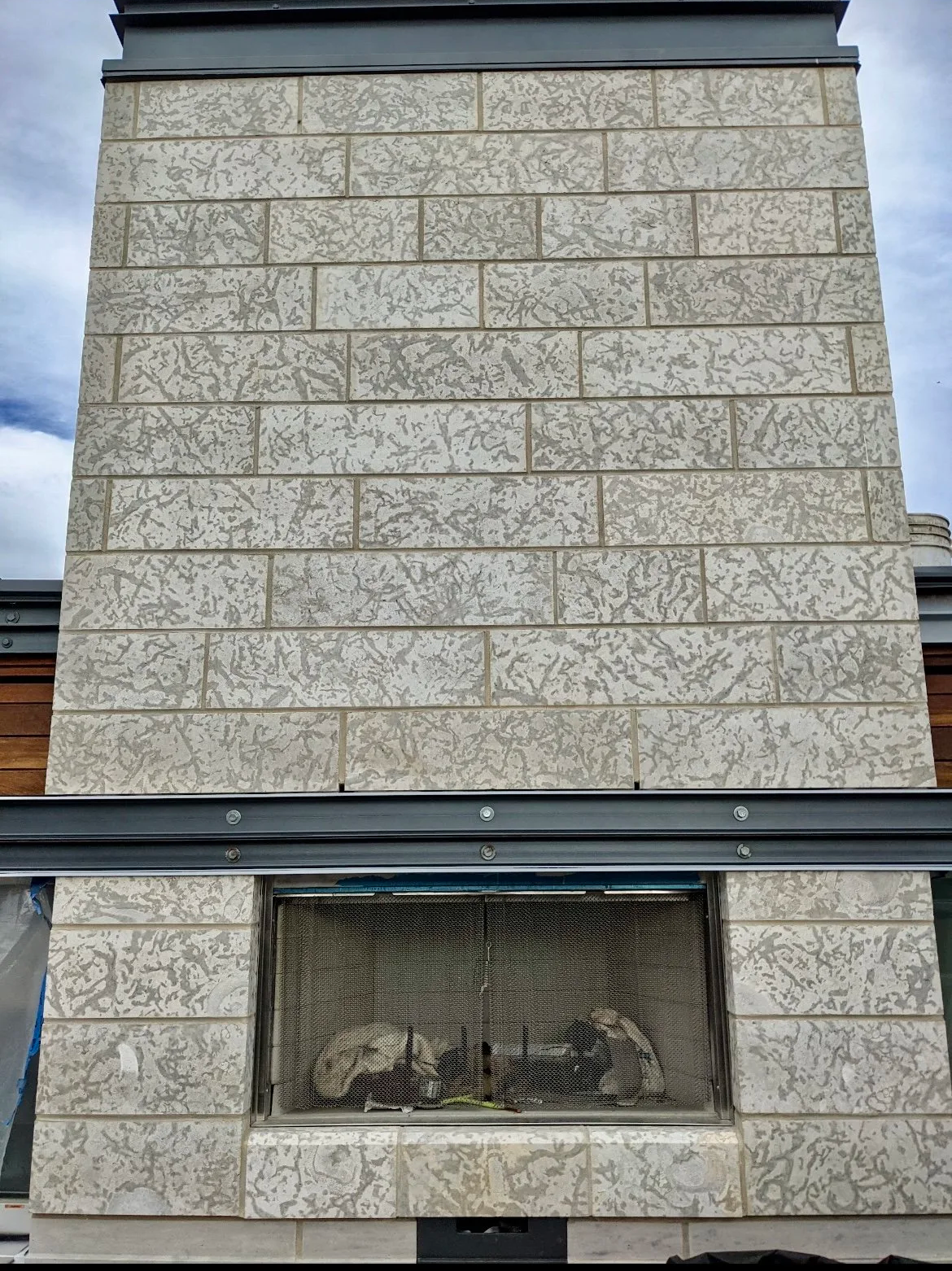 Outdoor brick fireplace with a chimney, gray stone tiles, and a protective mesh screen over the firebox.