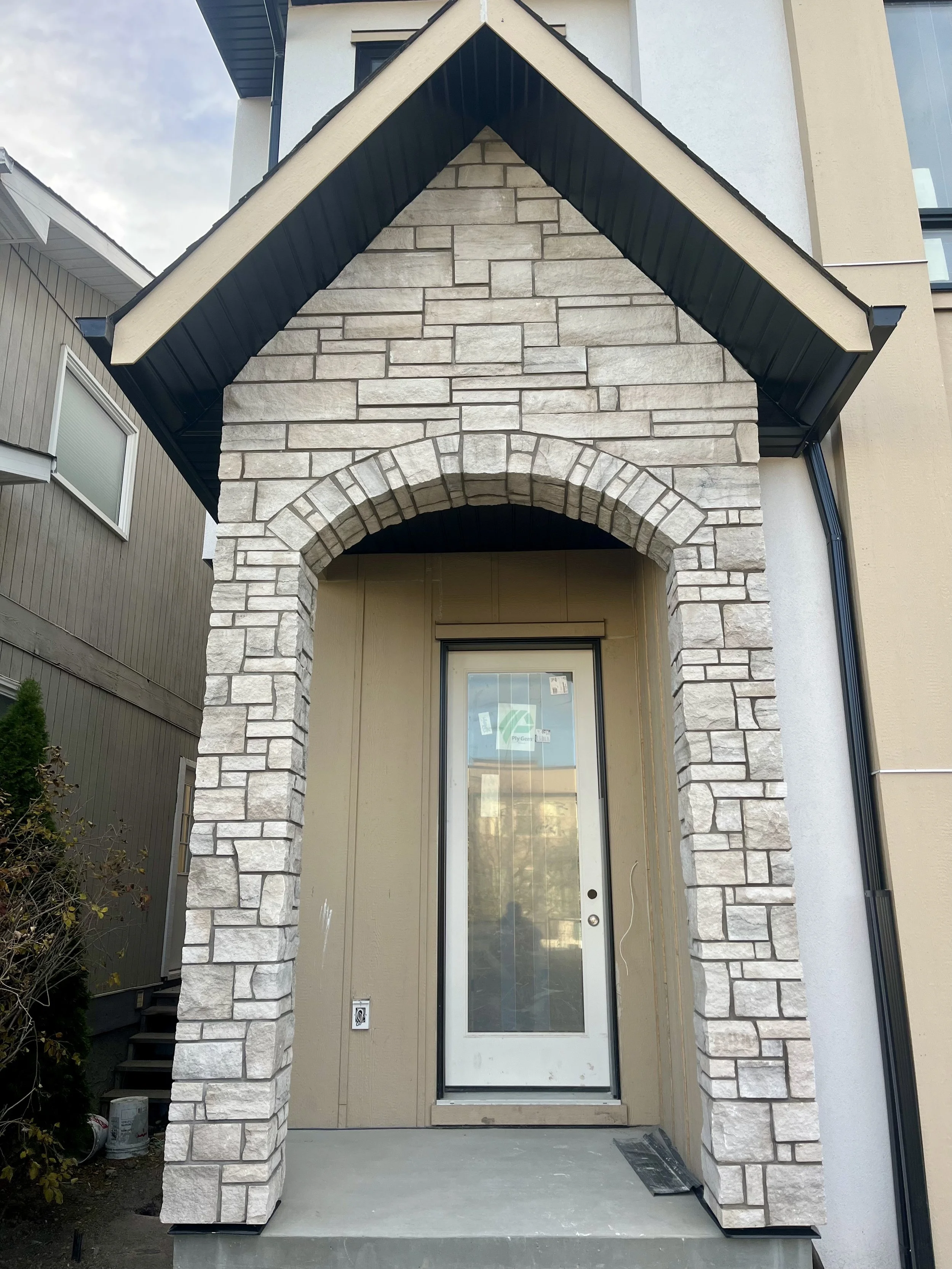 Newly built front entrance of a house with a stone archway and a door, under a gabled roof, in a suburban neighborhood.