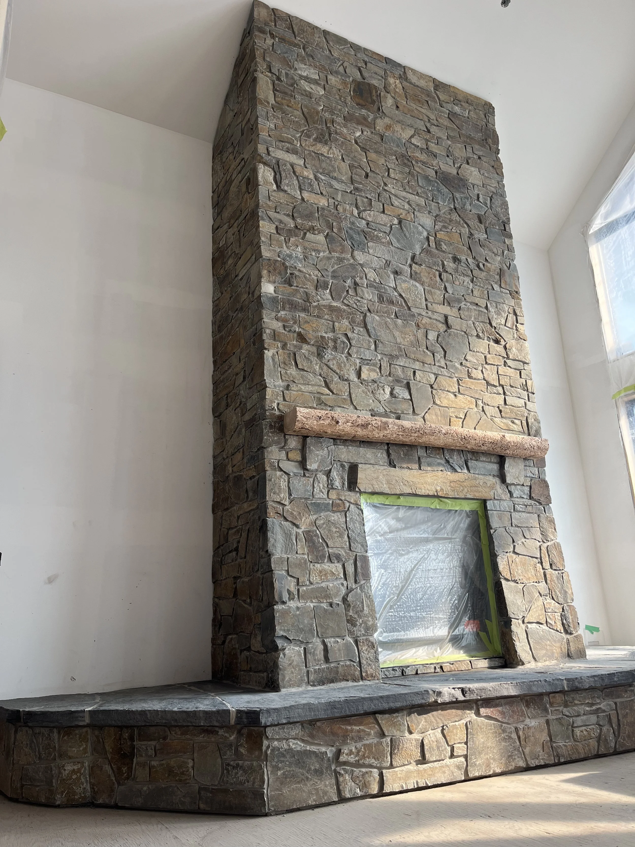 Stone fireplace under construction with a window and white wall