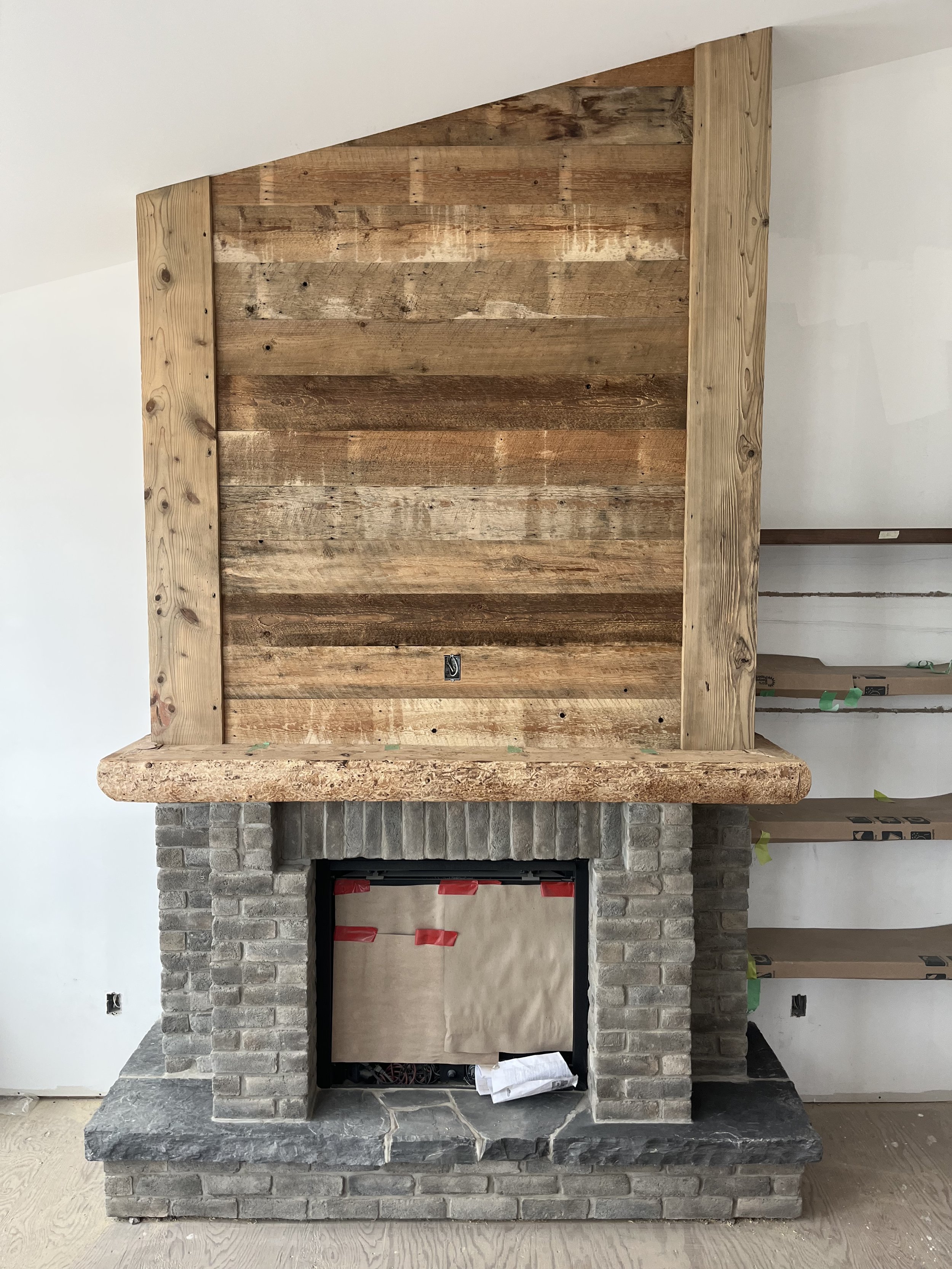Incomplete fireplace with a brick and stone surround, and a wooden panel above it under construction.