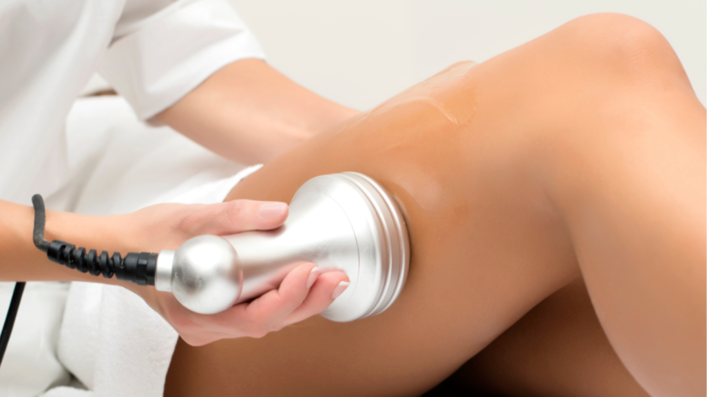 A medical professional uses a handheld device on a person's thigh during a treatment.