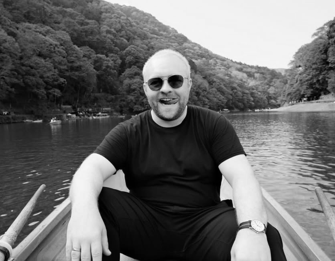 Black and white portrait of a man in a suit smiling, with a blurred office background.