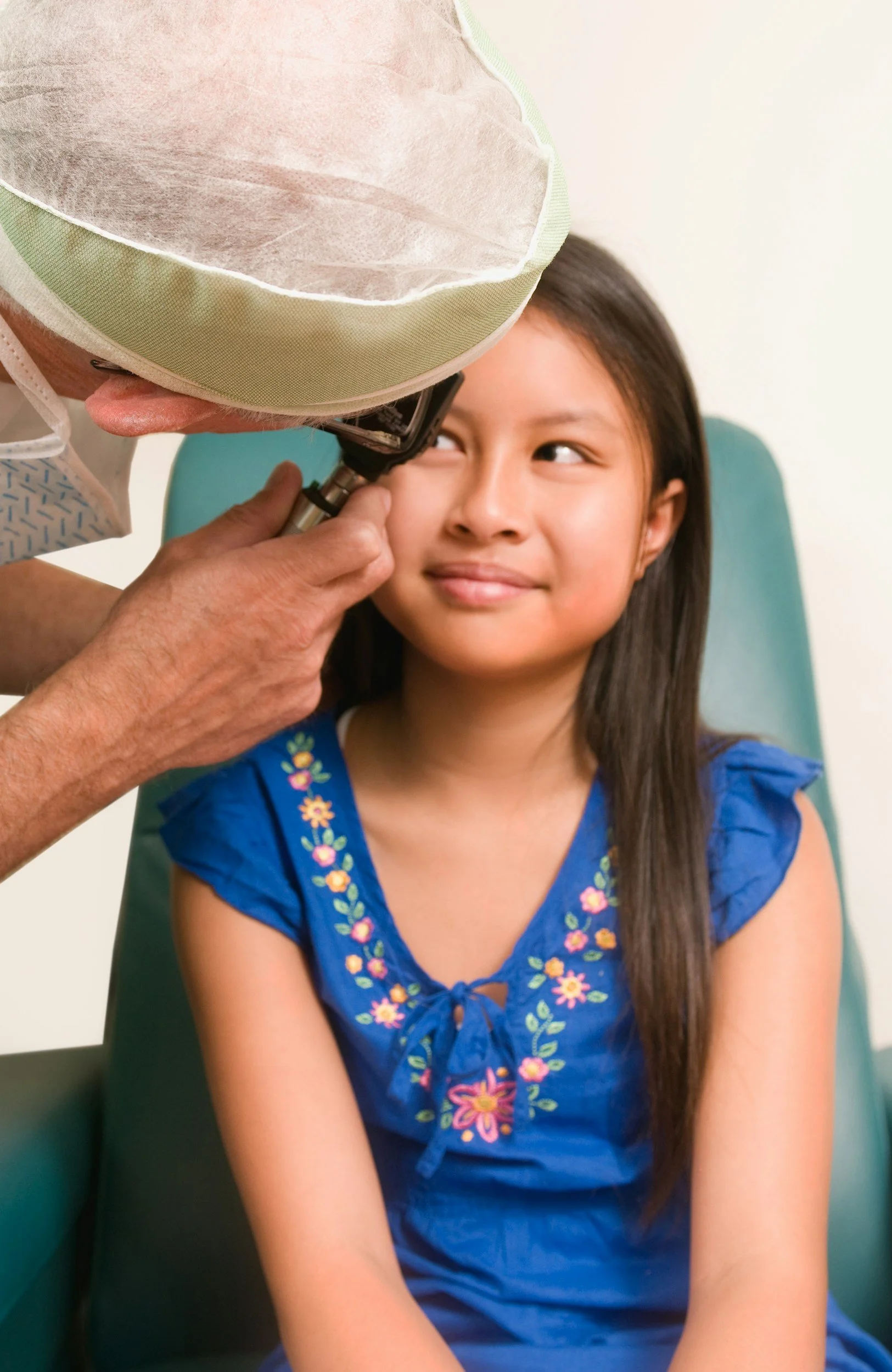 Doctor examining young girl’s ear with an otoscope in a medical setting.