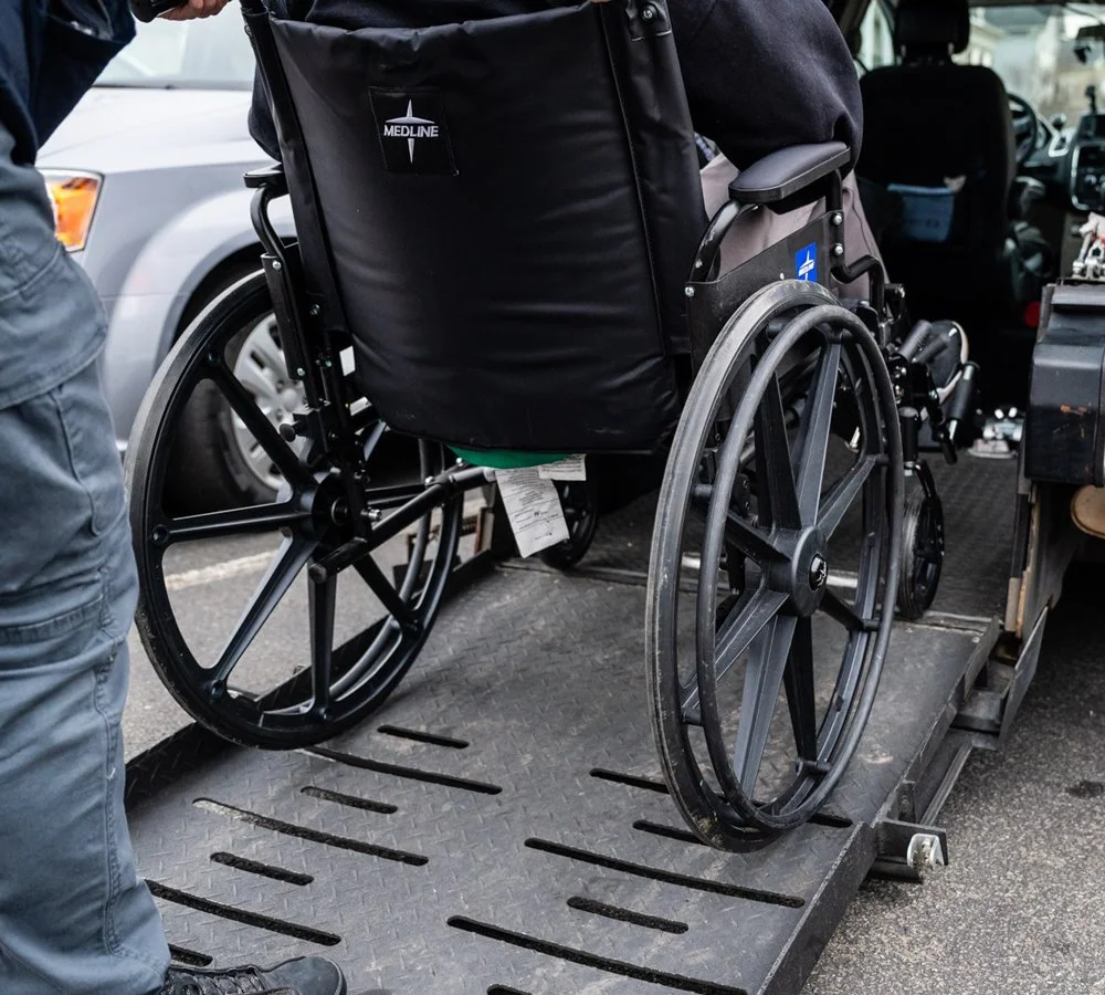 Wheelchair on a lift or ramp outside vehicle.
