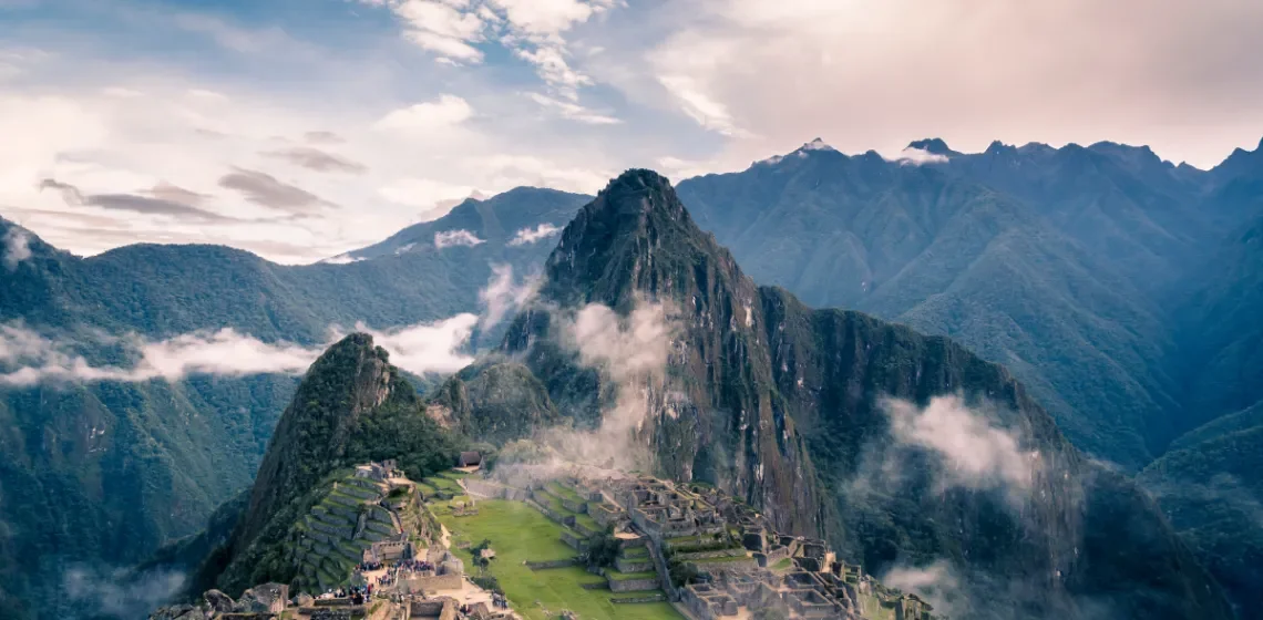 Ancient Incan city Machu Picchu nestled among green mountains with cloudy skies.