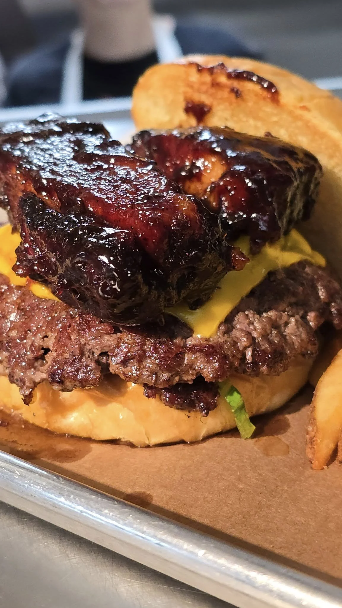 Close-up of a cheeseburger with barbecue ribs, melted cheddar cheese, lettuce, and a toasted bun, served with potato fries.