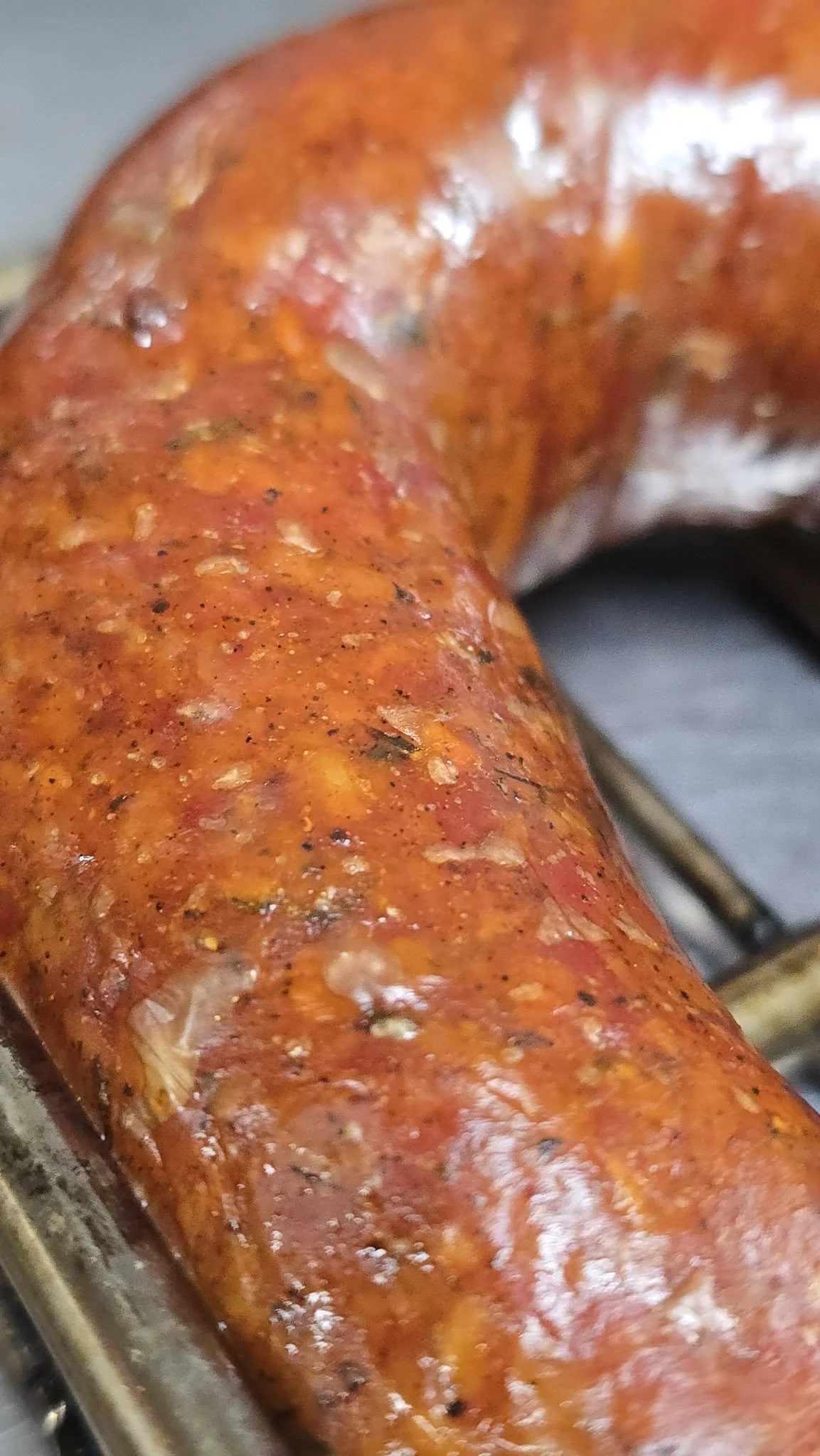 Close-up of a cooked sausage link with a reddish-brown, seasoned, and slightly crispy exterior.