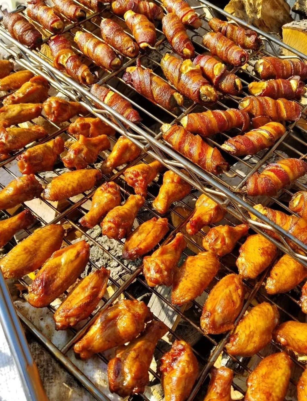 Rows of grilled bacon-wrapped jalapeño peppers and glazed chicken wings on a cooking grill.