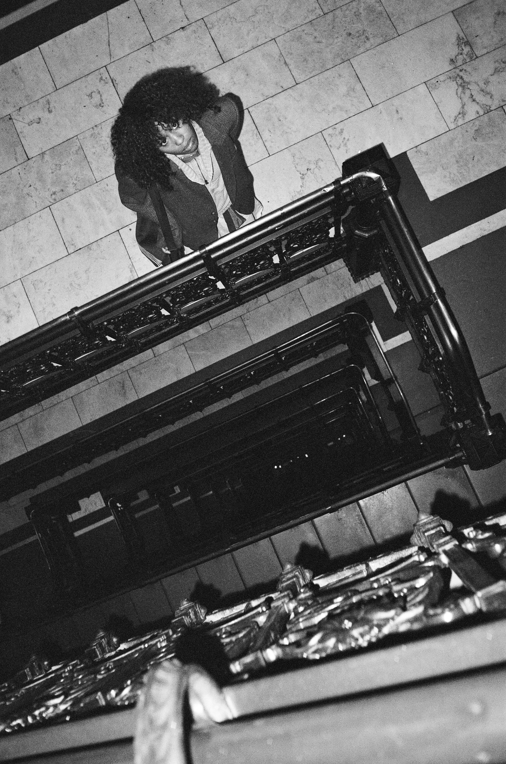 A woman with curly hair is standing and looking up at the camera, taken from below near the staircase.