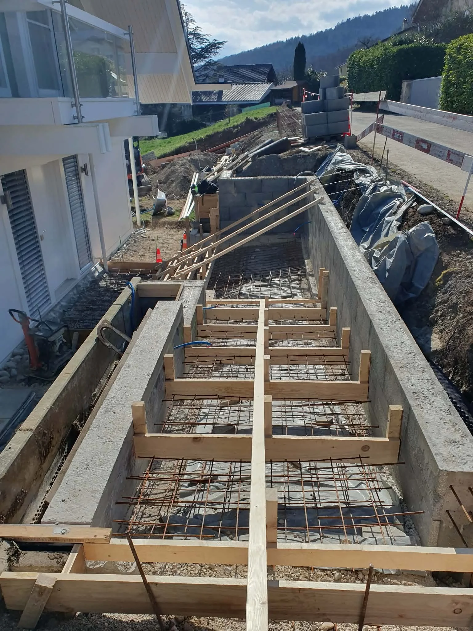 Travaux de construction de fondation avec barres d'armature, bois et béton en préparation, autour d'une maison résidentielle