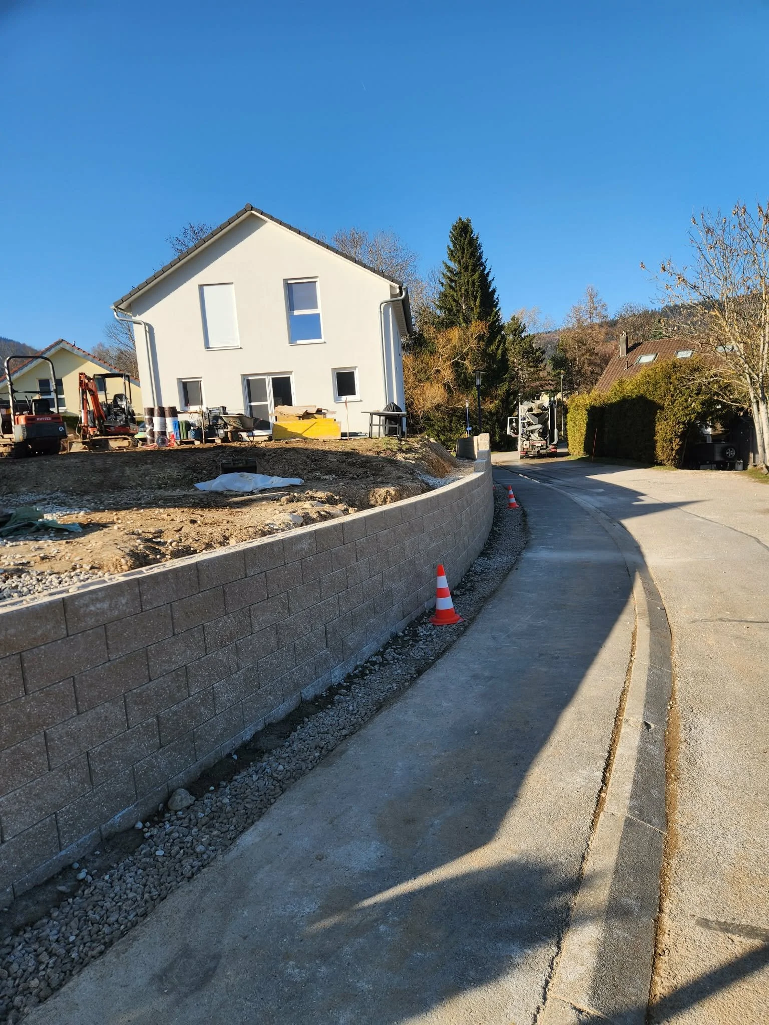 Construction d'une nouvelle maison avec une clôture en béton et des travaux en cours, panneaux de signalisation de construction, sous un ciel bleu clair.